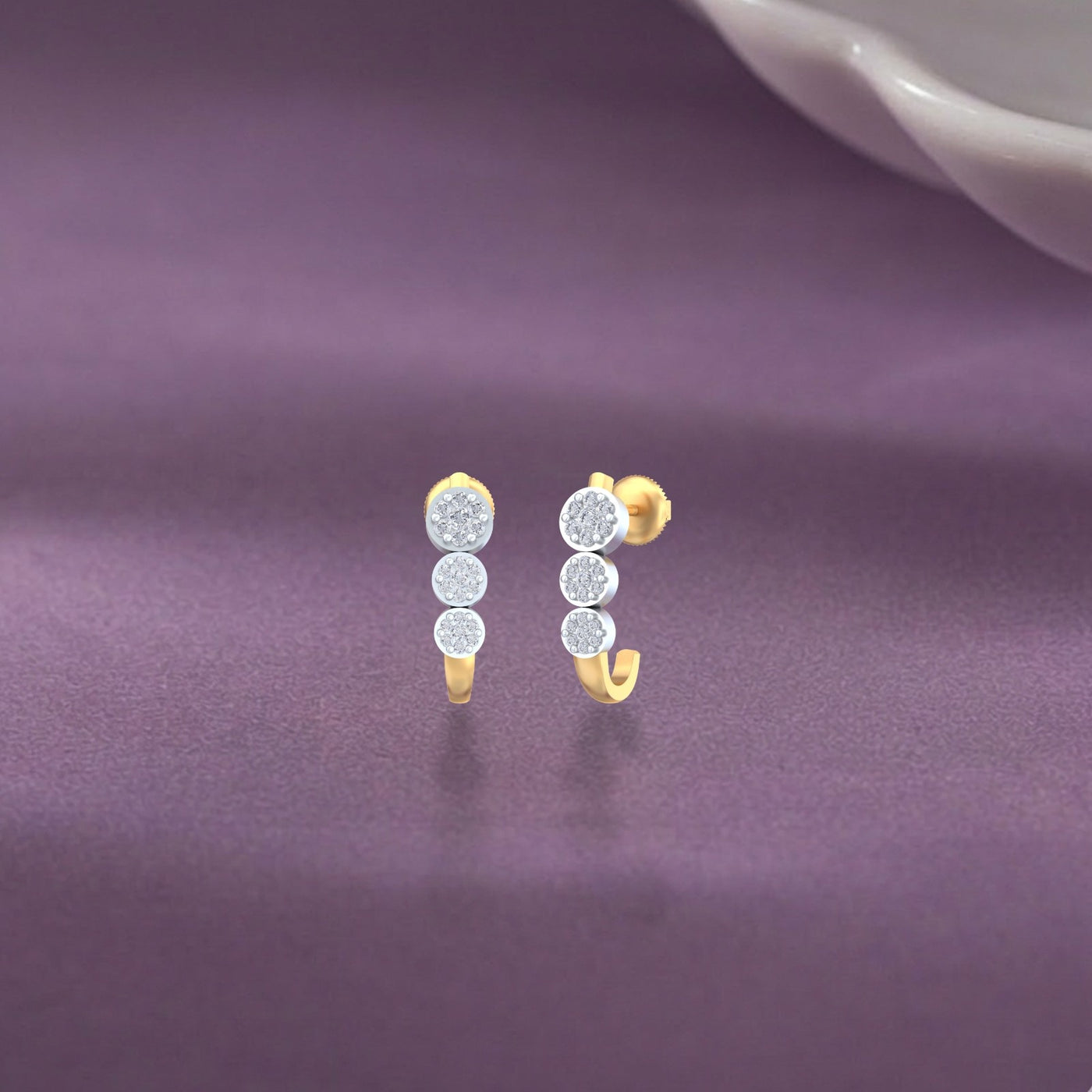 Gold and diamond half hoop earring on a purple surface.