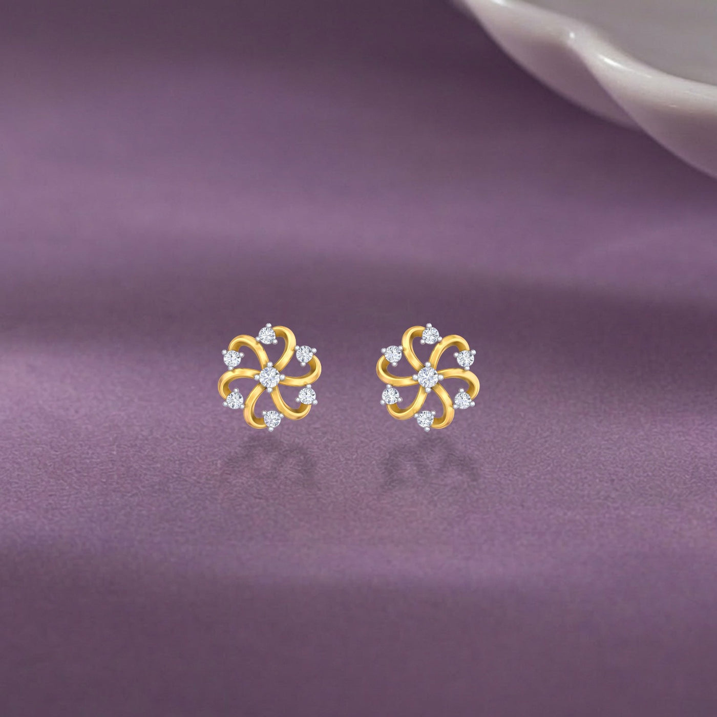 Gold and diamond floral stud earrings on a purple fabric background