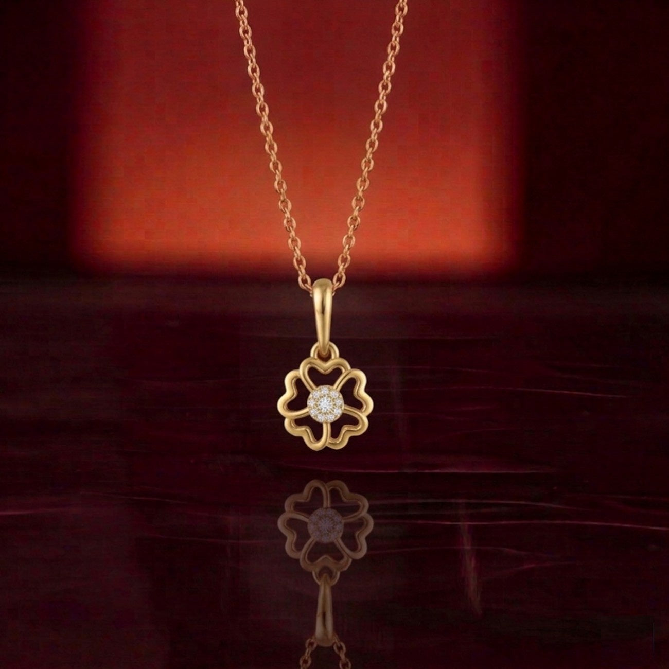 Gold necklace with a floral pendant on a reflective surface with a red background