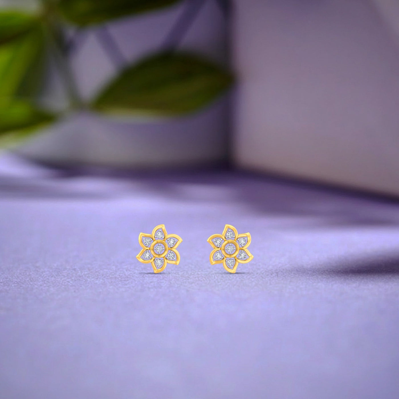 Gold and diamond flora stud earrings on a light purple surface.