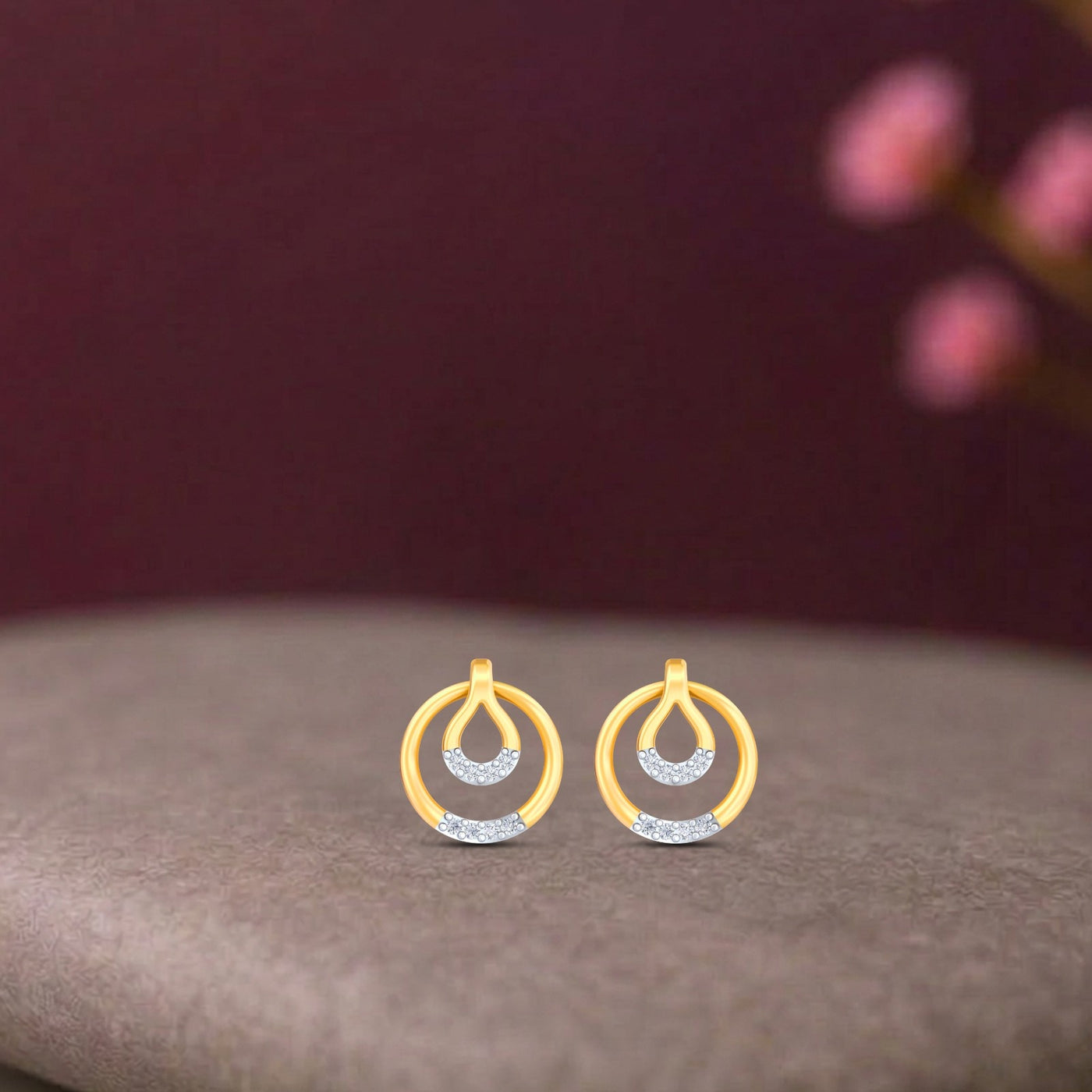 Gold and diamond earrings with circular design on a beige surface.