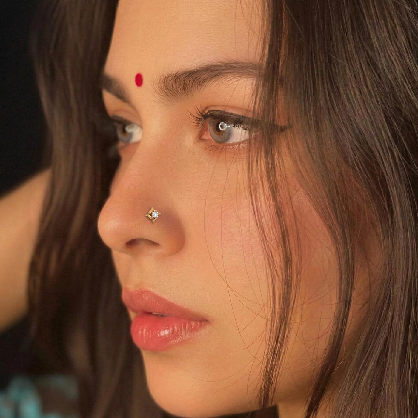 Close-up of a woman's face with a diamond nose pin and red bindi.