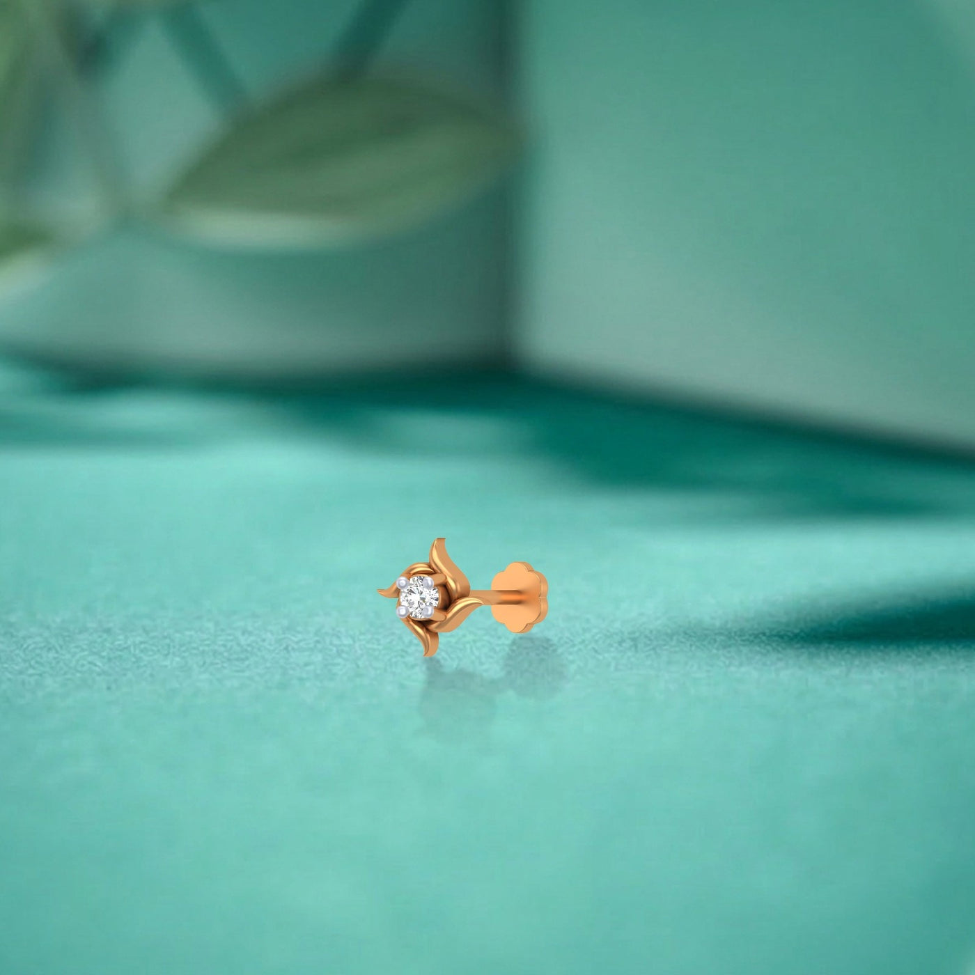 Yellow gold and diamond stud nose pin on a teal surface
