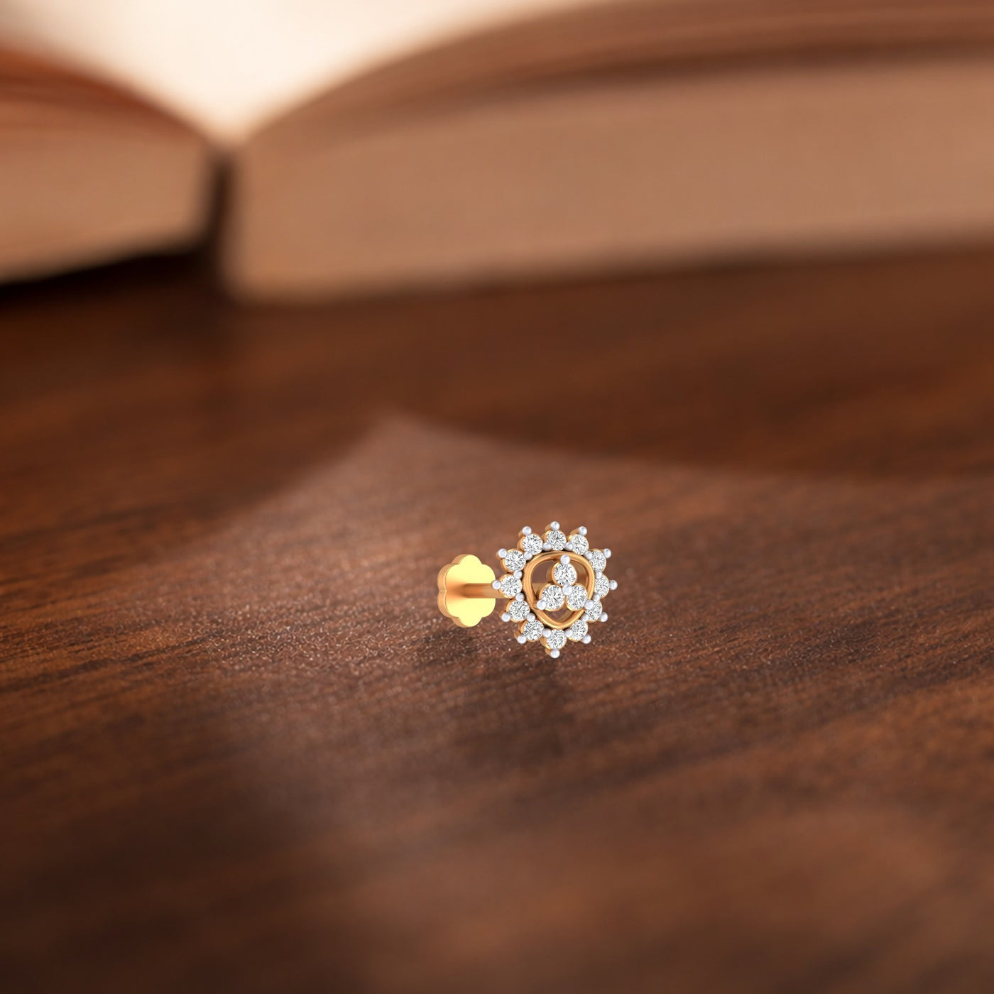 Yellow gold and diamond stud nose pin on a wooden surface with a blurred book in the background.