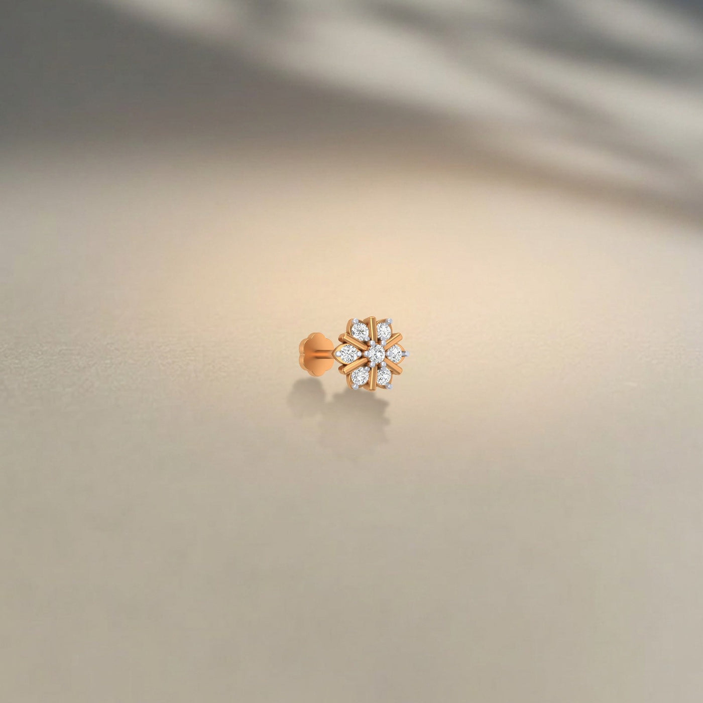 Gold and diamond stud nosepin with floral-shaped on a beige background.