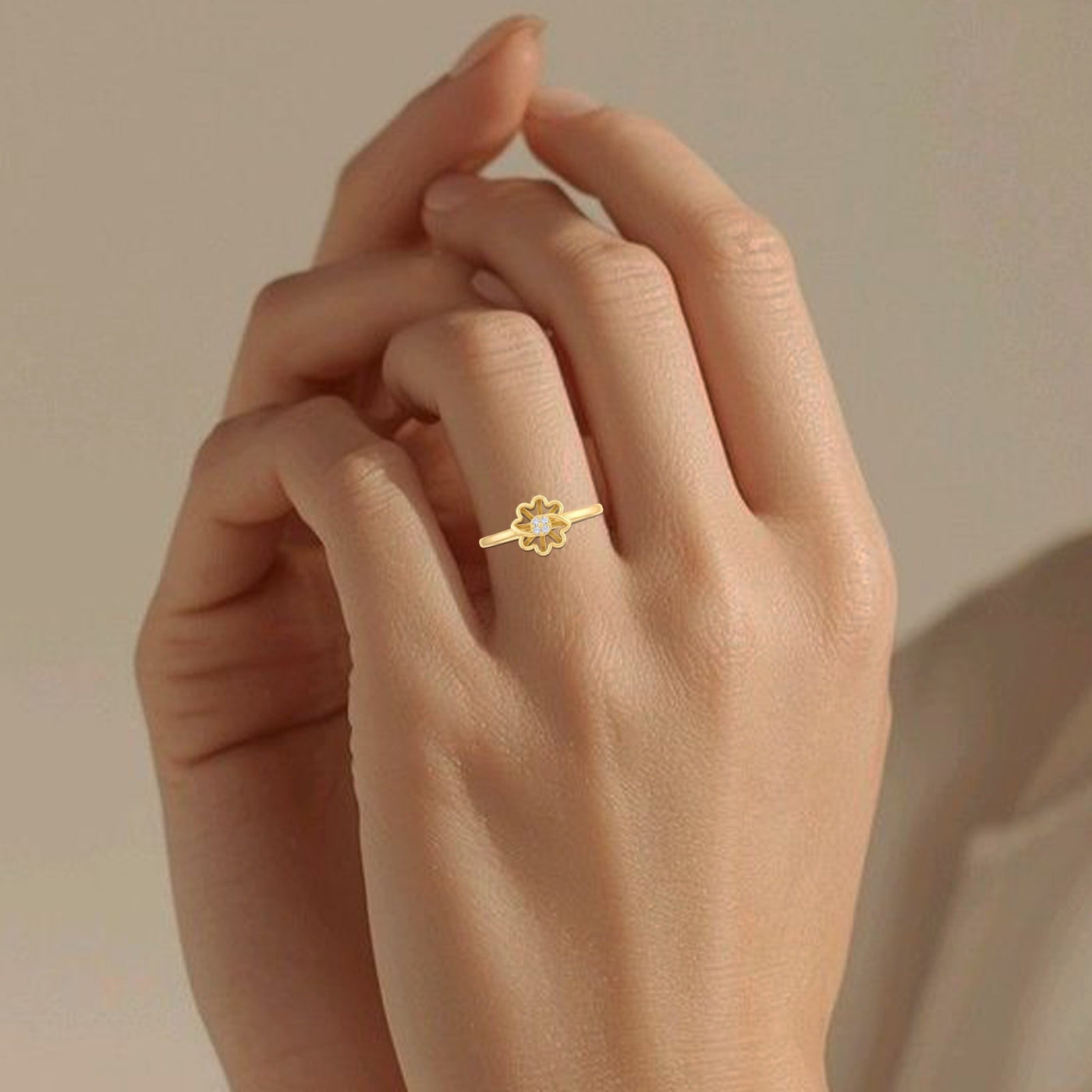 Hand wearing a gold ring with a flower design on a beige background