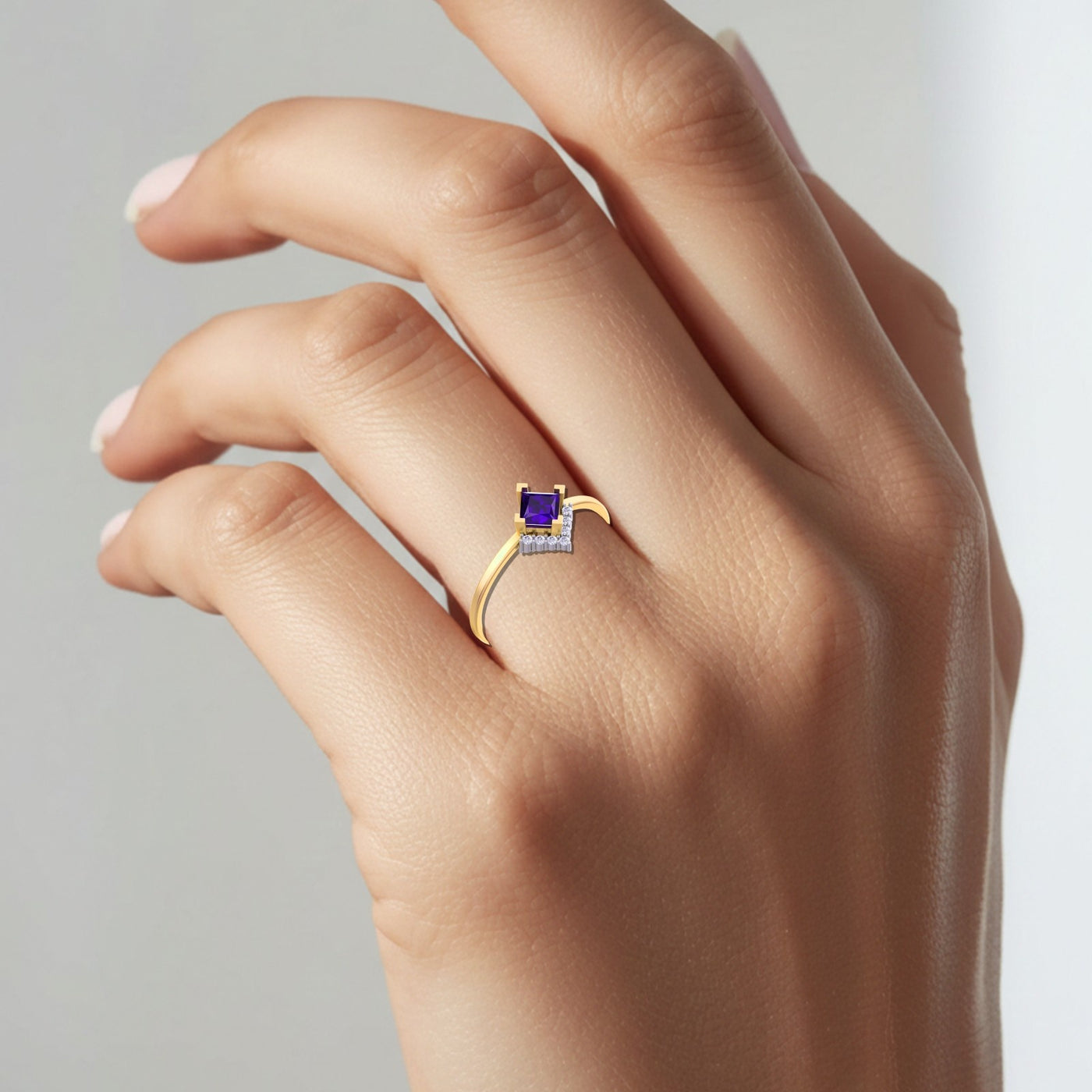 Gold ring with a purple gemstone on a hand against a gray background