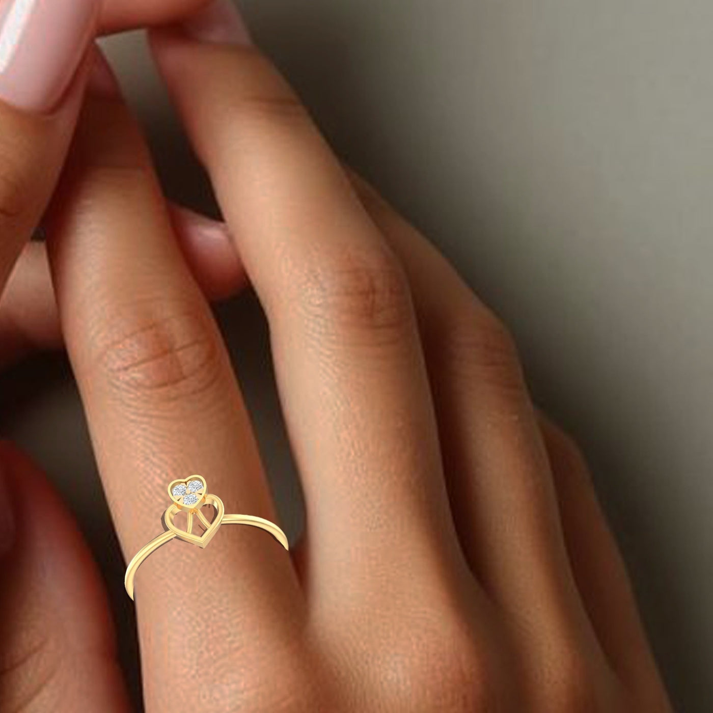 Gold ring with a heart design and gemstone on a person's finger against a neutral background