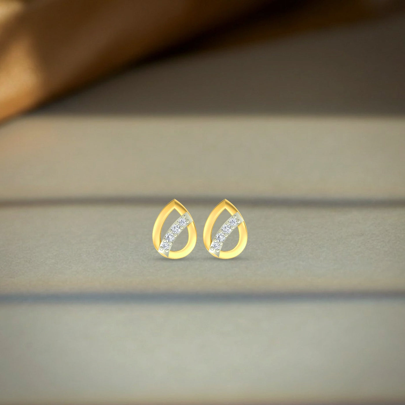 Gold and diamond pear-shaped earrings on a beige fabric background
