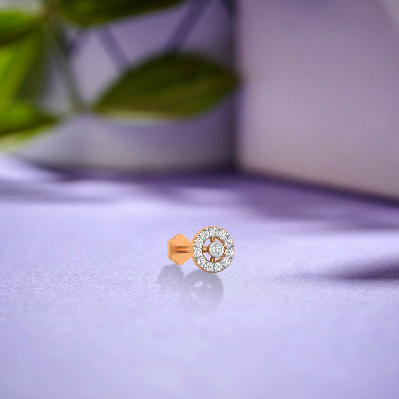 Yellow gold and diamond stud nose pin on a light purple surface 