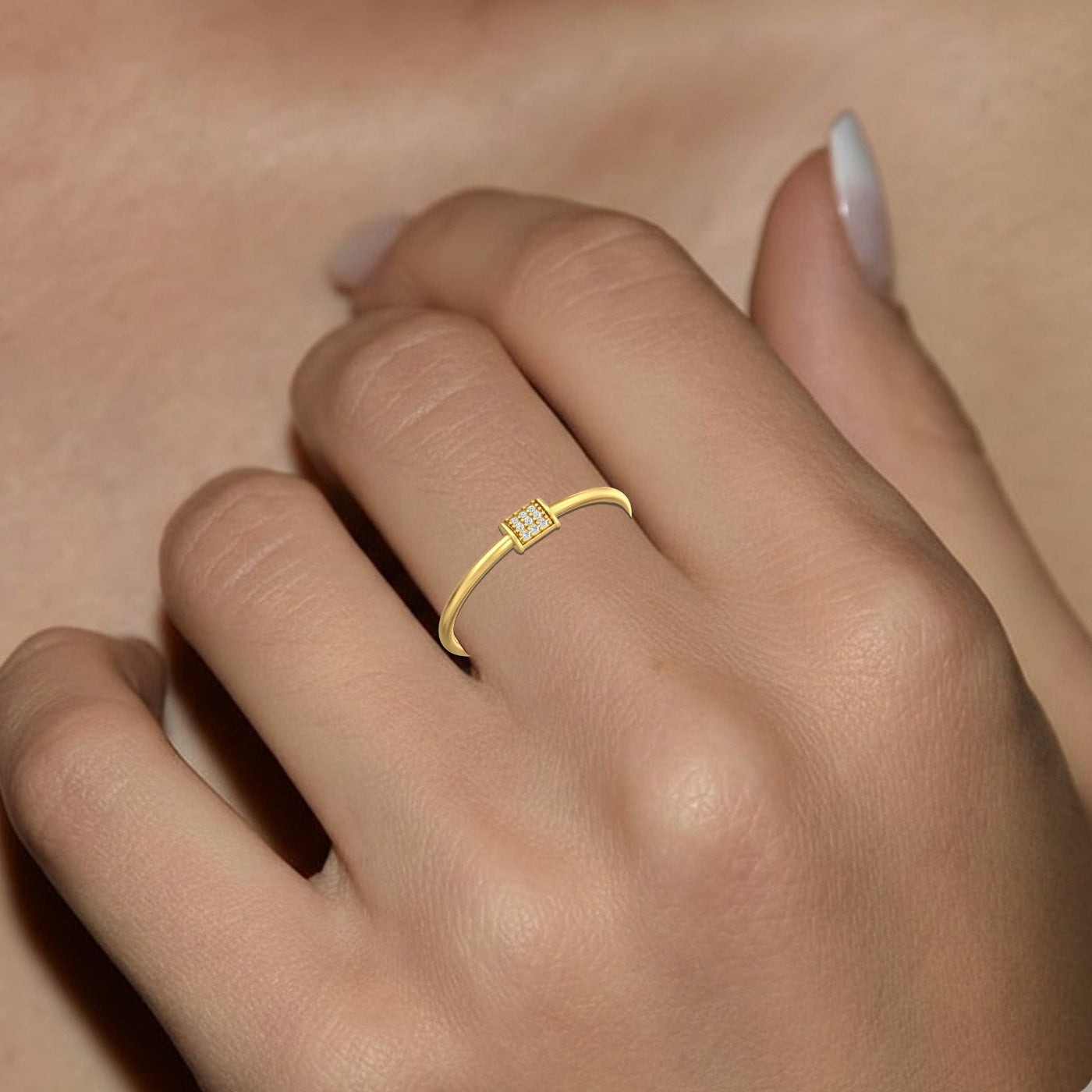 Gold ring with small diamonds on a person's finger against a neutral background