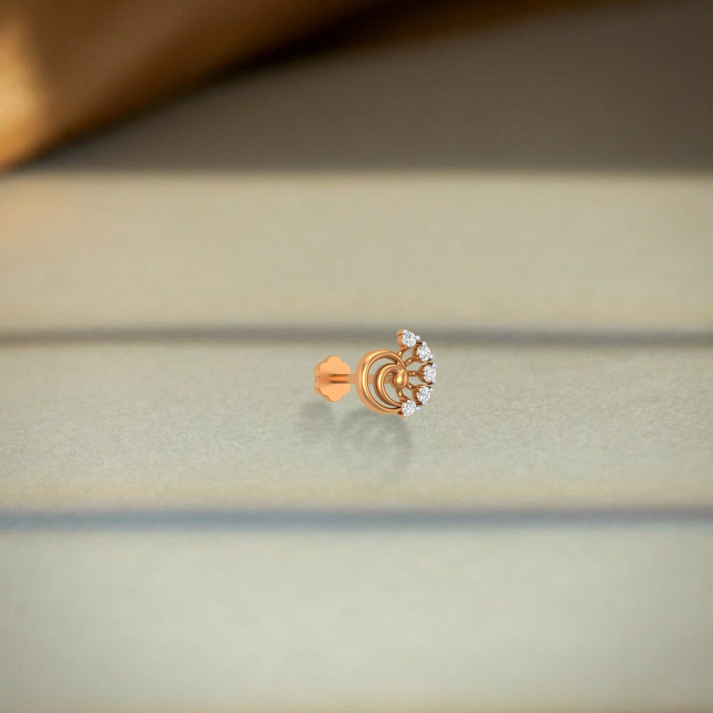 yellow gold and diamond stud nose pin with floral design on a light fabric background