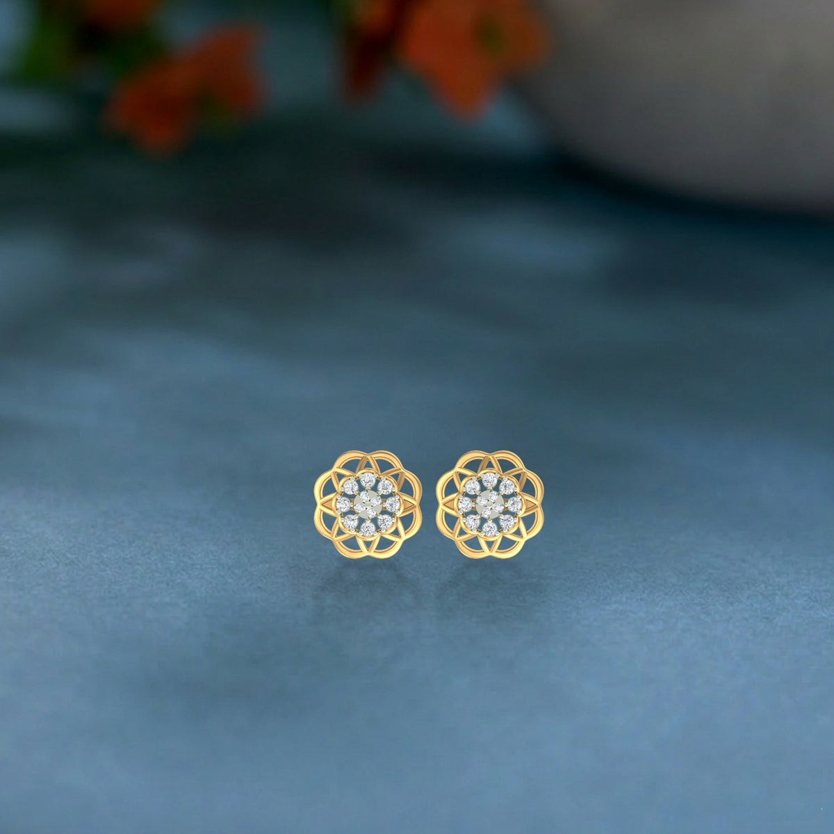 Gold and diamond stud earring with floral-design on a blue surface.