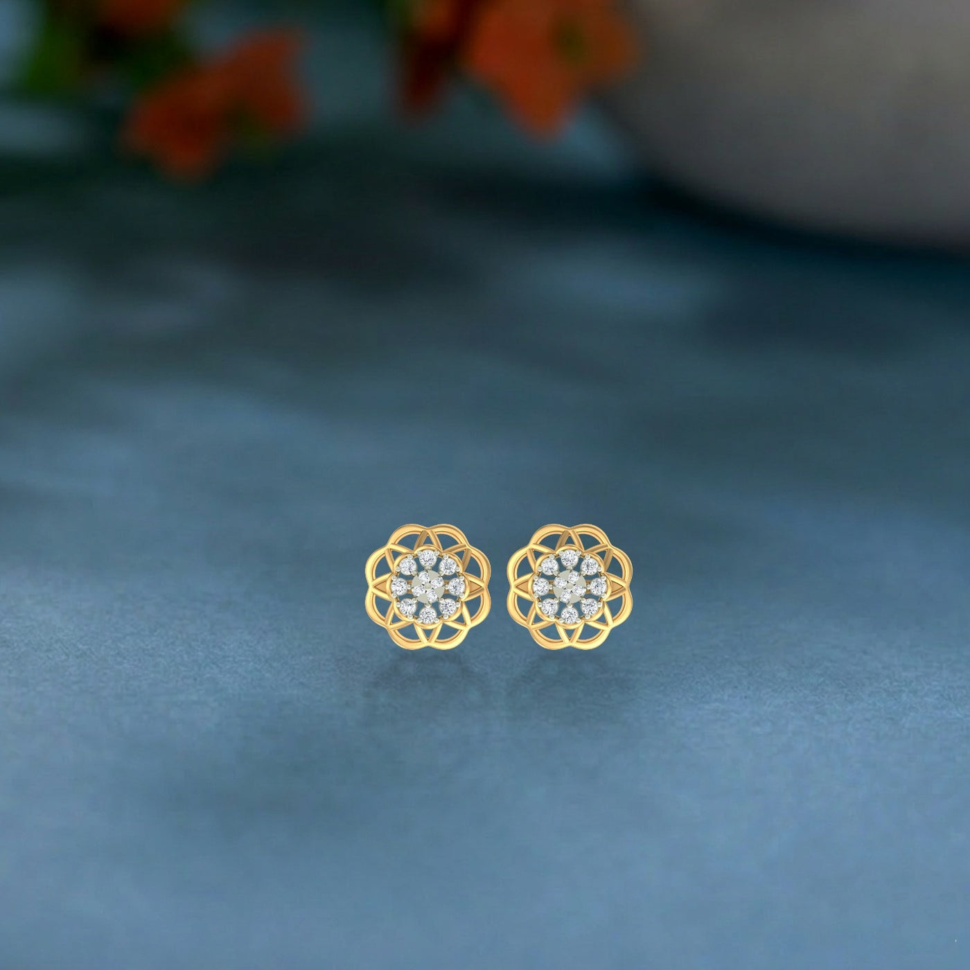 Gold and diamond stud earring with floral-design on a blue surface.