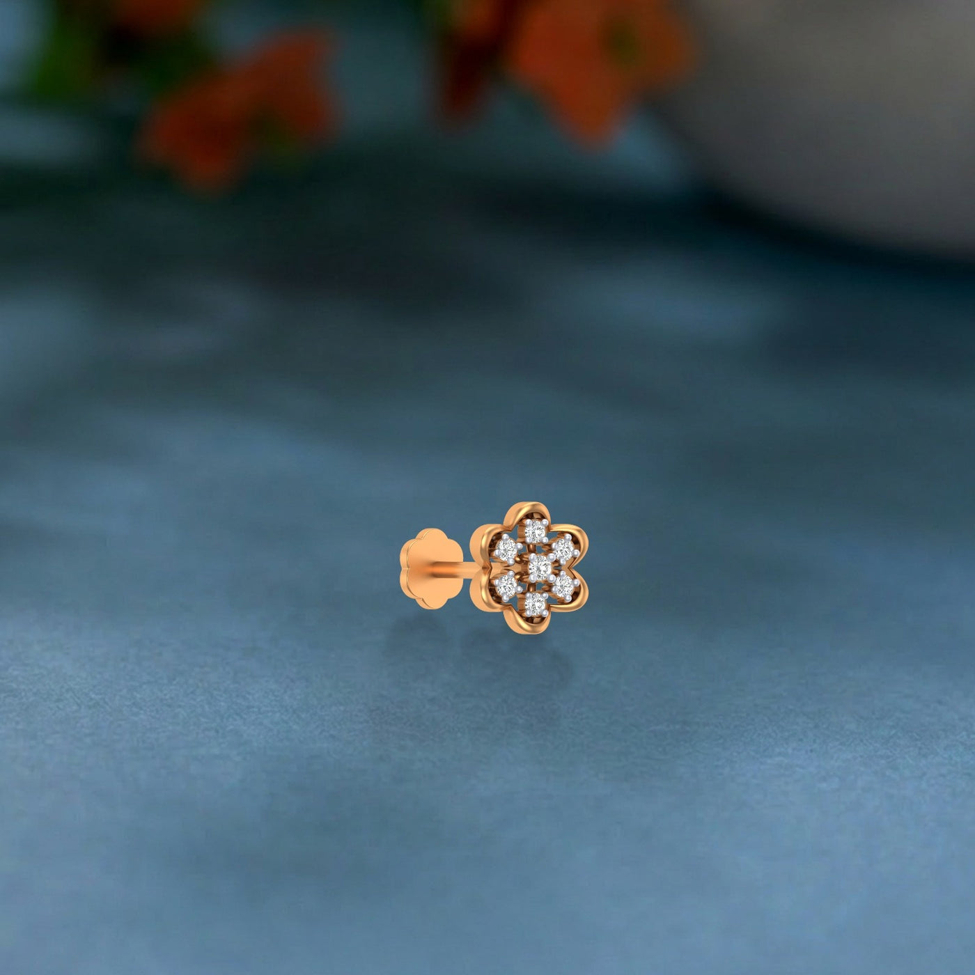 yellow gold and diamond stud nose pin on a blue surface with a blurred floral background