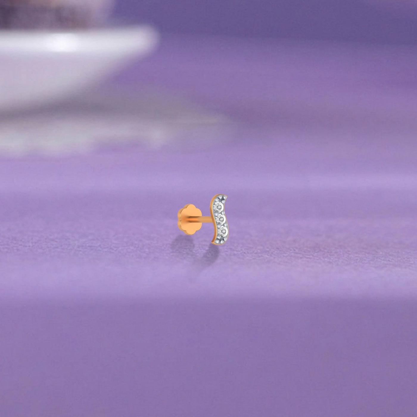 Yellow gold and diamond stud nose pin with clear stones on a purple surface