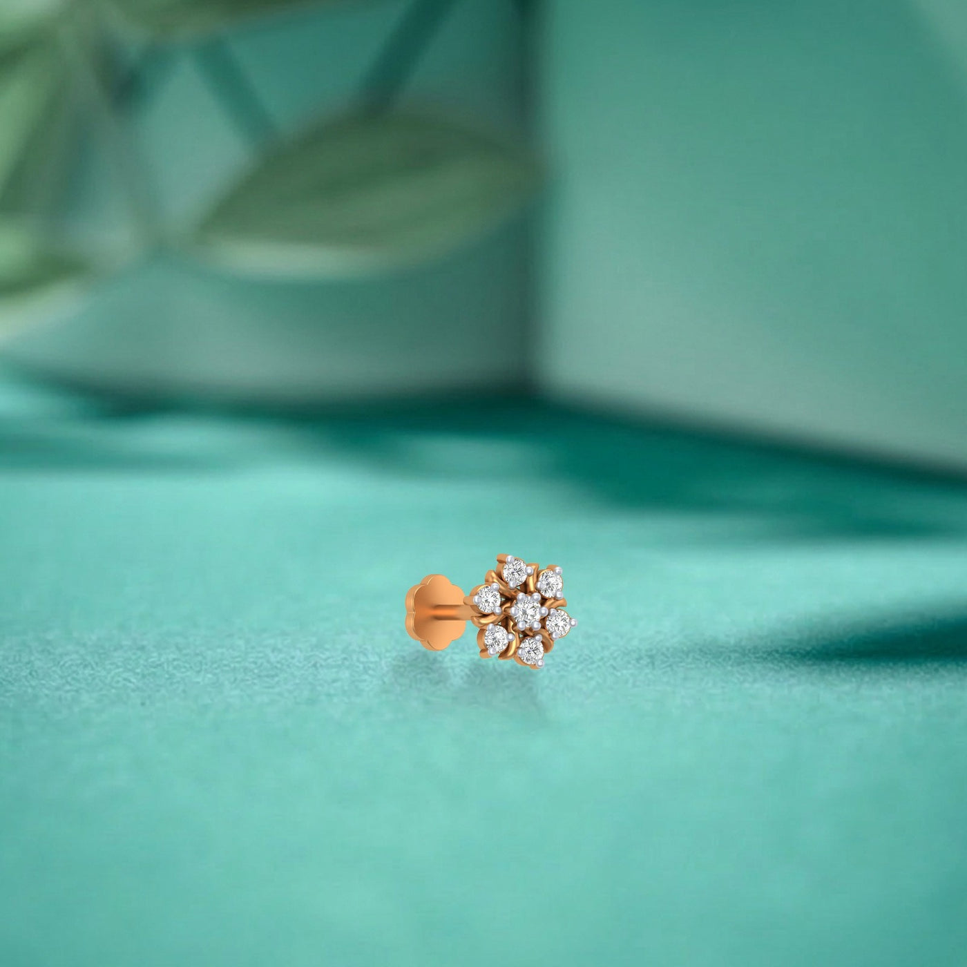 yellow gold and diamond stud nose pin with clear gemstones on a teal fabric background