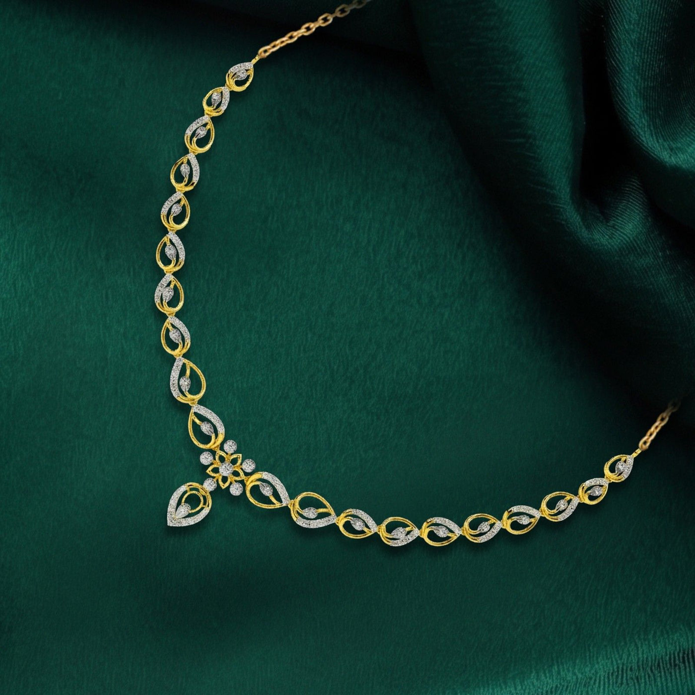 A gold and diamond necklace with a floral and teardrop design, displayed on a draped dark green satin fabric.
