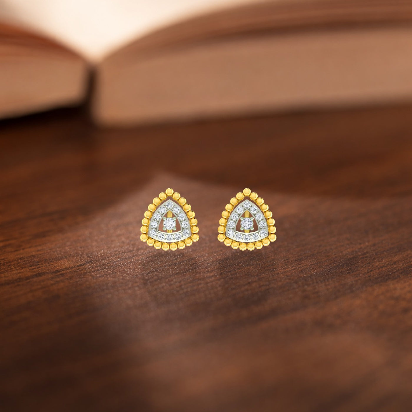 Gold and diamond triangle halo stud earrings on a wooden surface.