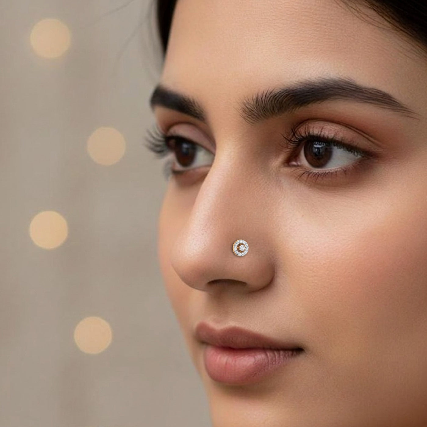 Close-up portrait of a woman wearing a small, round gold and diamond nose stud on her nostril, set against a softly blurred background with warm bokeh lights.