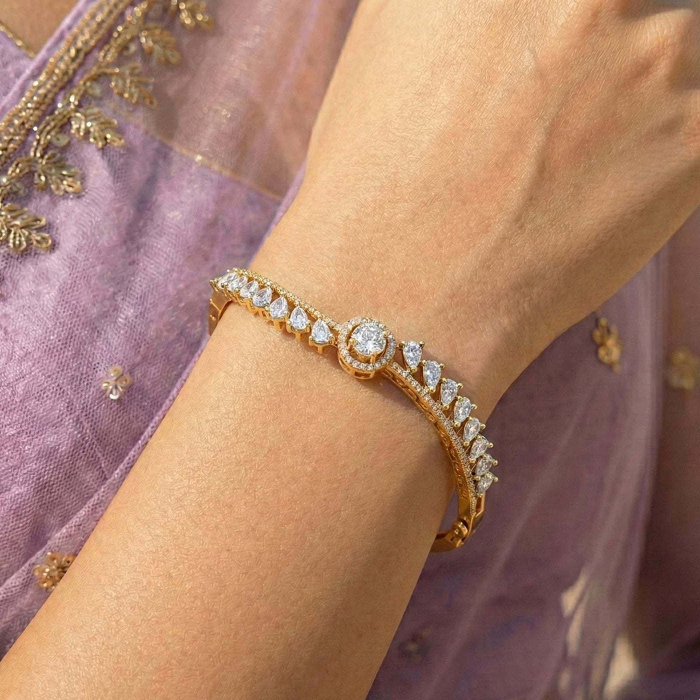 Yellow gold bangle bracelet with round halo diamond centerpiece and pear-cut diamond accents.