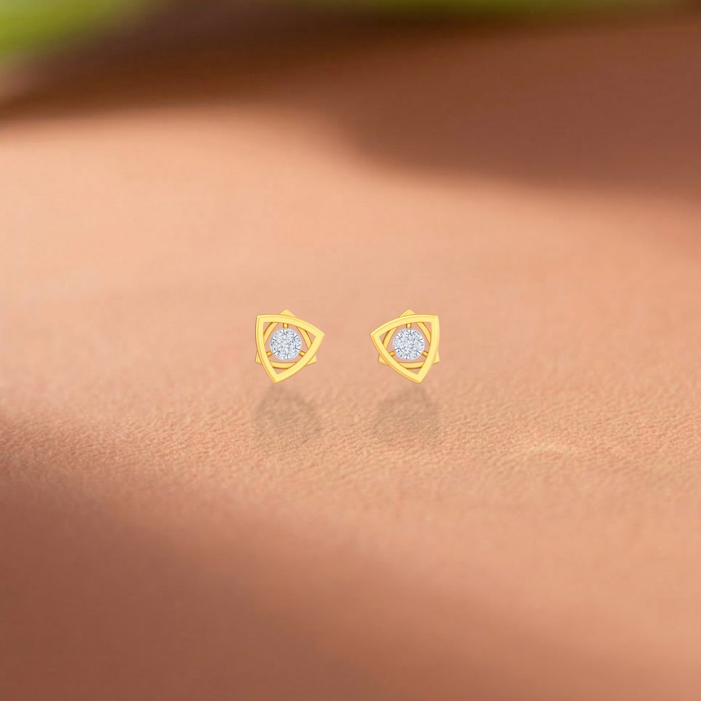 Gold and diamond stud earrings on a pink surface.