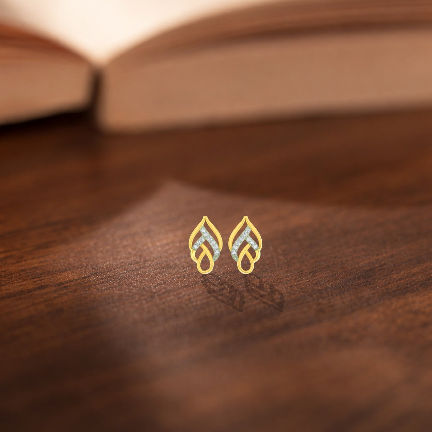Gold and diamond leaf-design earrings on a wooden surface.