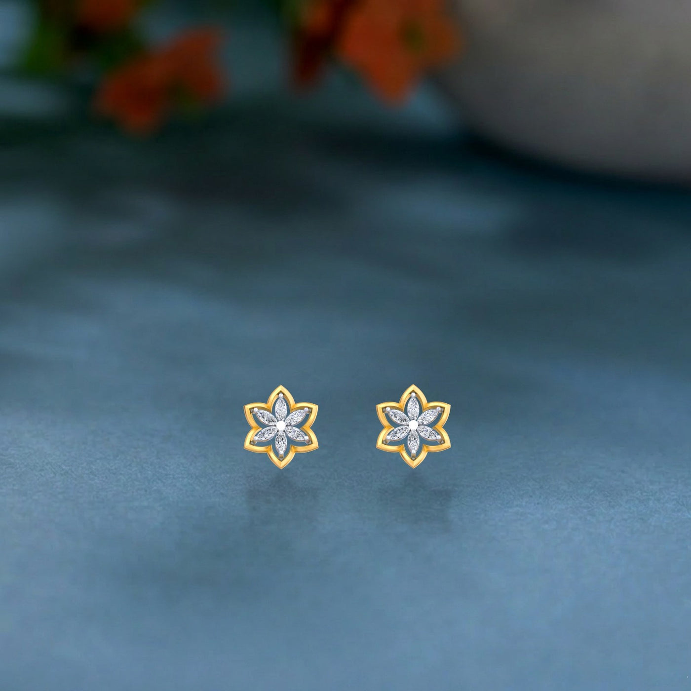 Pair of gold and diamond flower-shaped earrings on a blue surface.