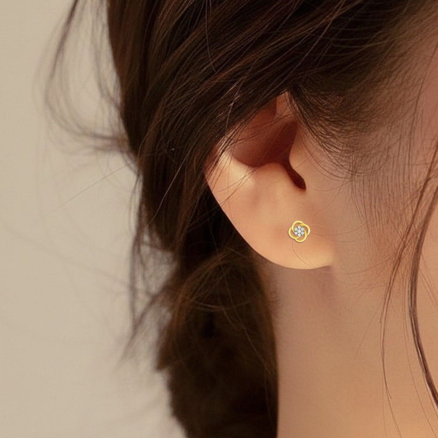 Close-up of an ear wearing a gold and diamond floral stud earring.