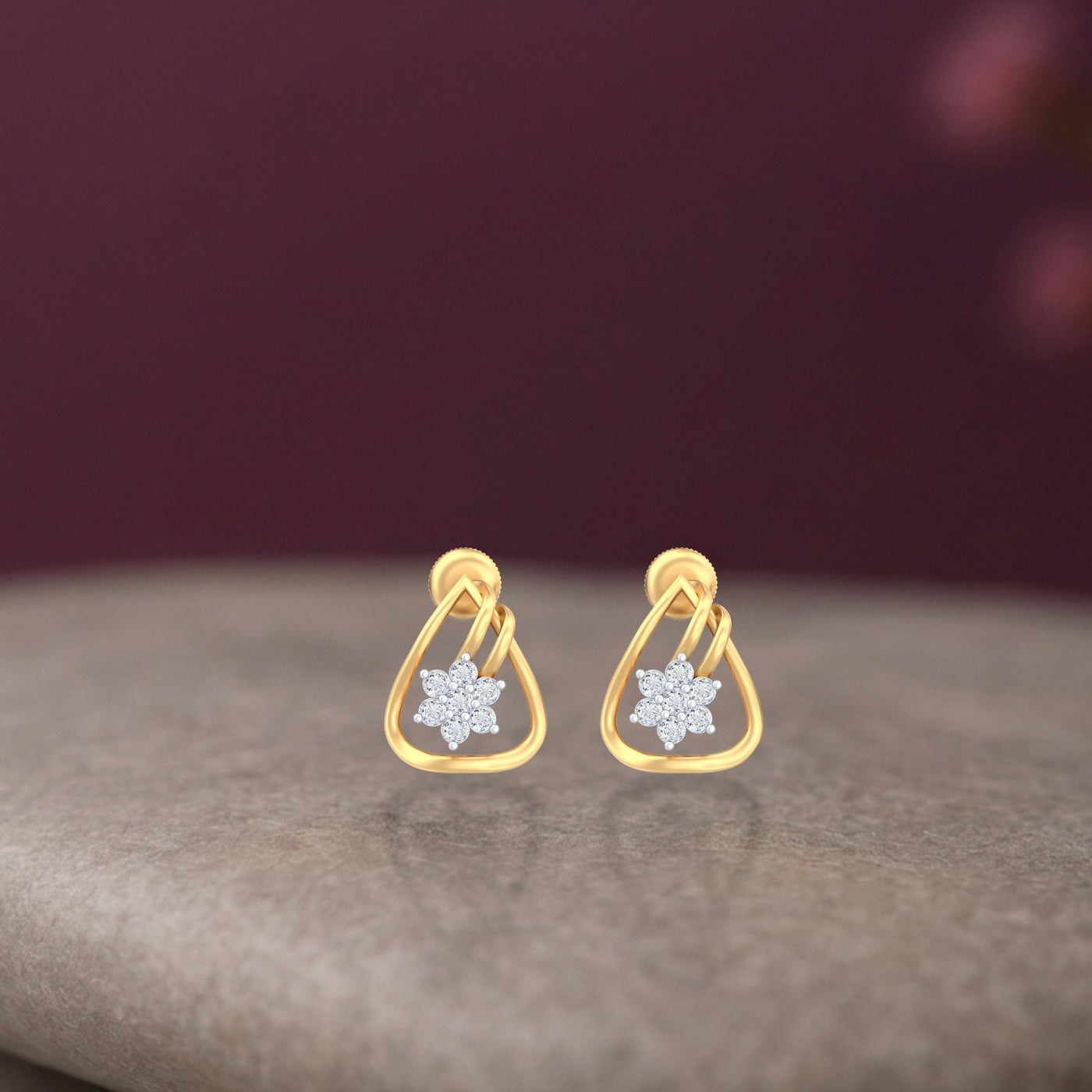 Gold and diamond stud earrings with floral design on a texture surface.