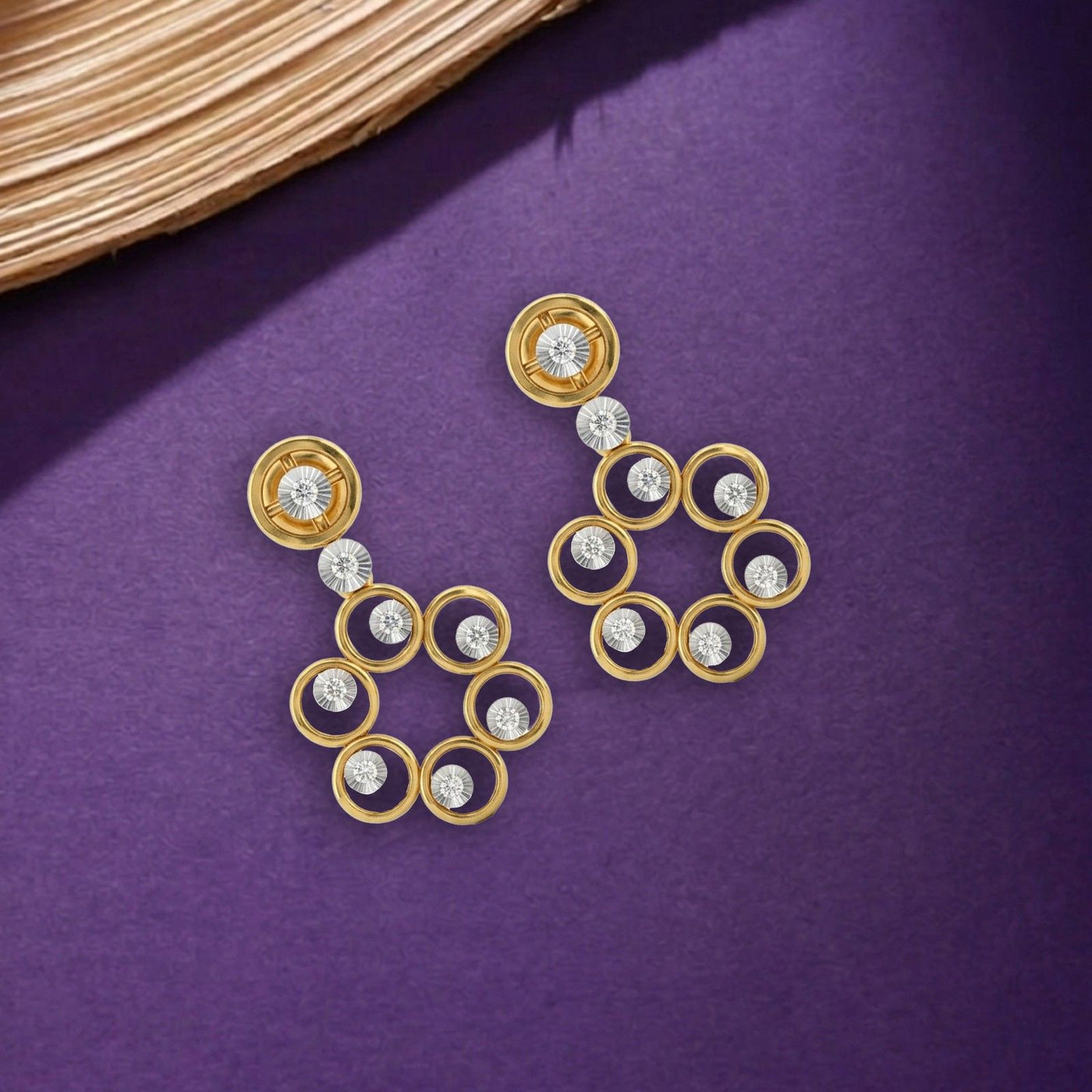Gold and diamond drop earrings on a purple surface