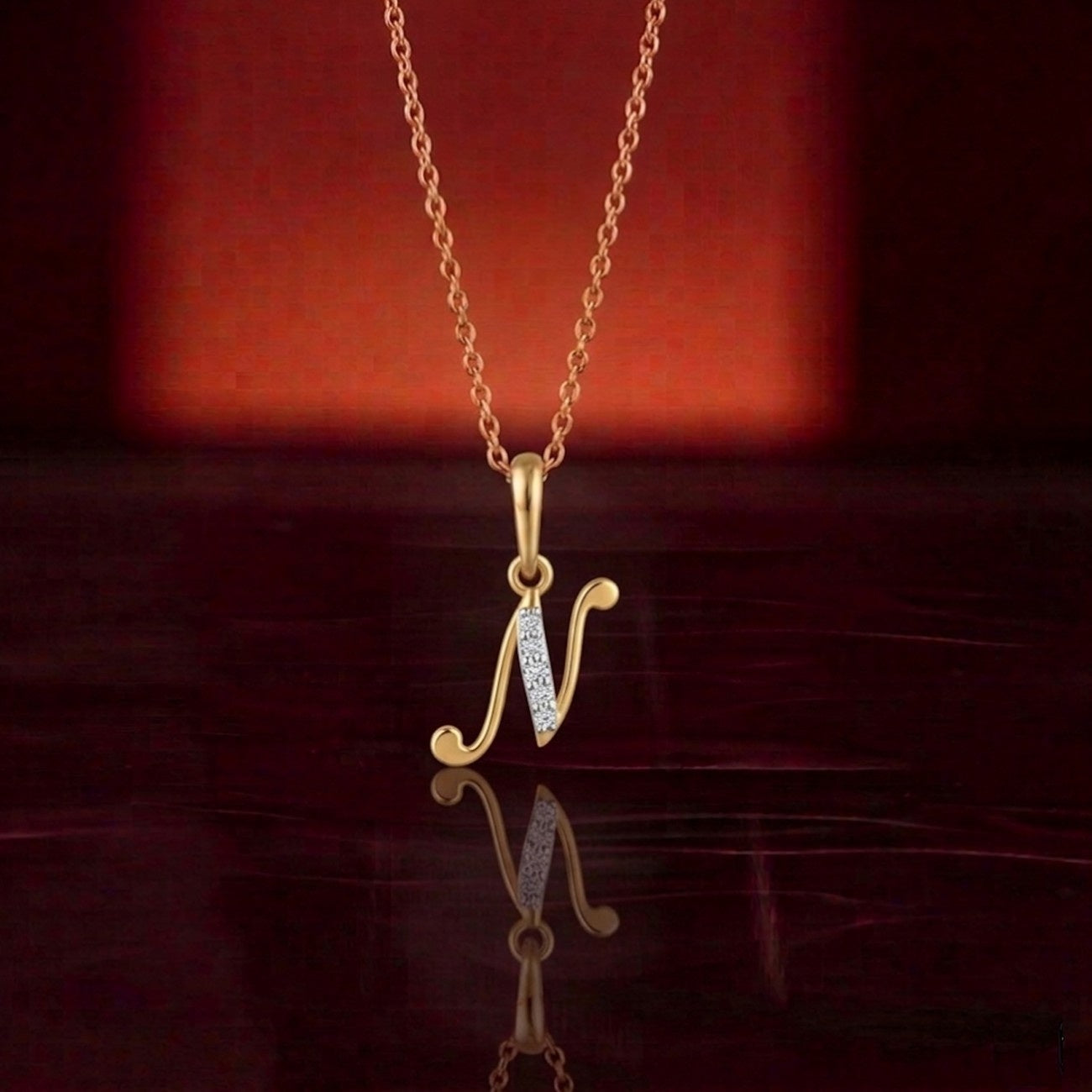 Gold necklace with a 'N' pendant on a reflective surface with a red background