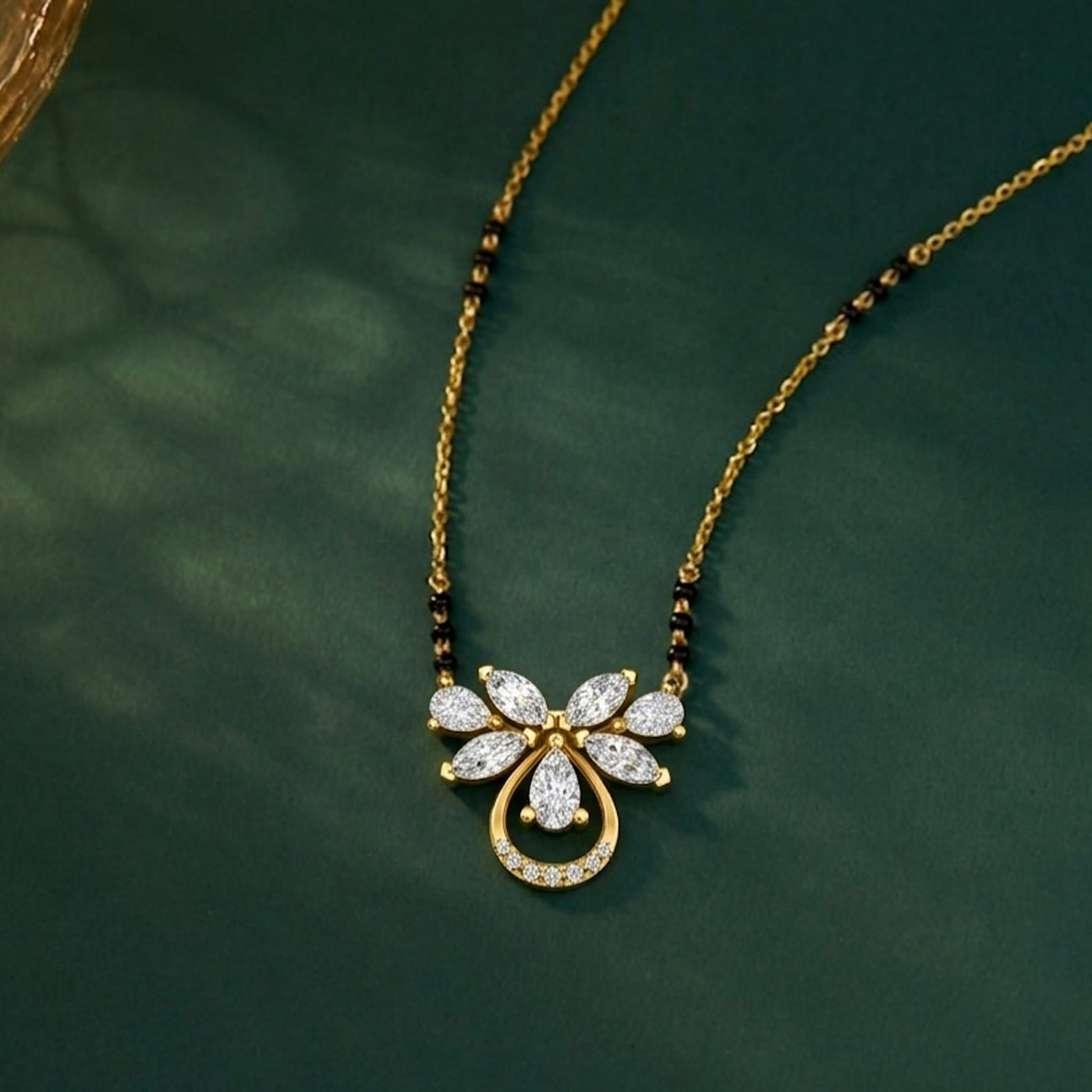 A gold and diamond mangalsutra with a butterfly set with clear stones, displayed on a dark green textured background.