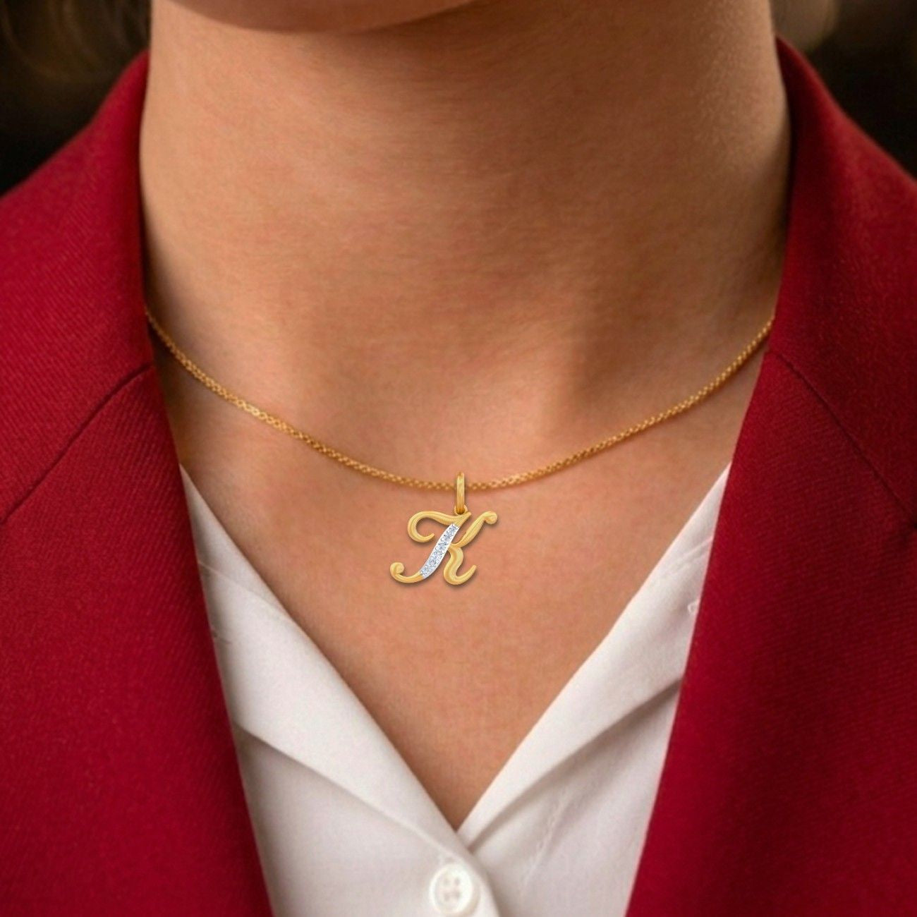Gold necklace with a letter 'K' pendant worn by a person in a red blazer and white shirt.