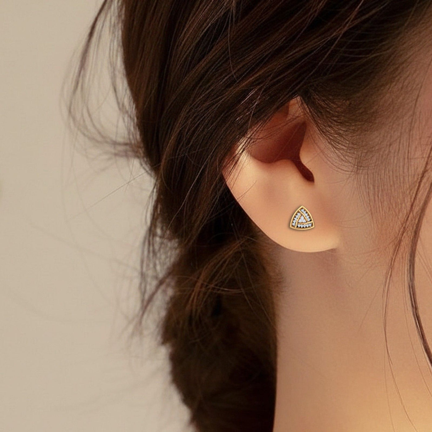 Close-up shot of a gold and diamond stud earring with triangle-shaped.