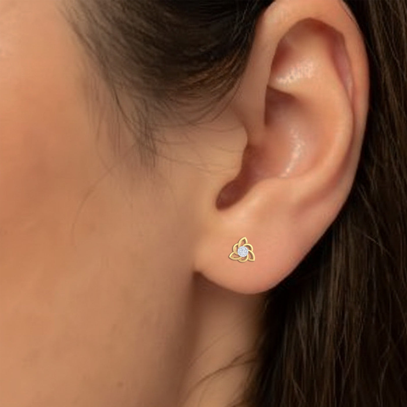 Close-up of an ear wearing a gold and diamond stud earring.