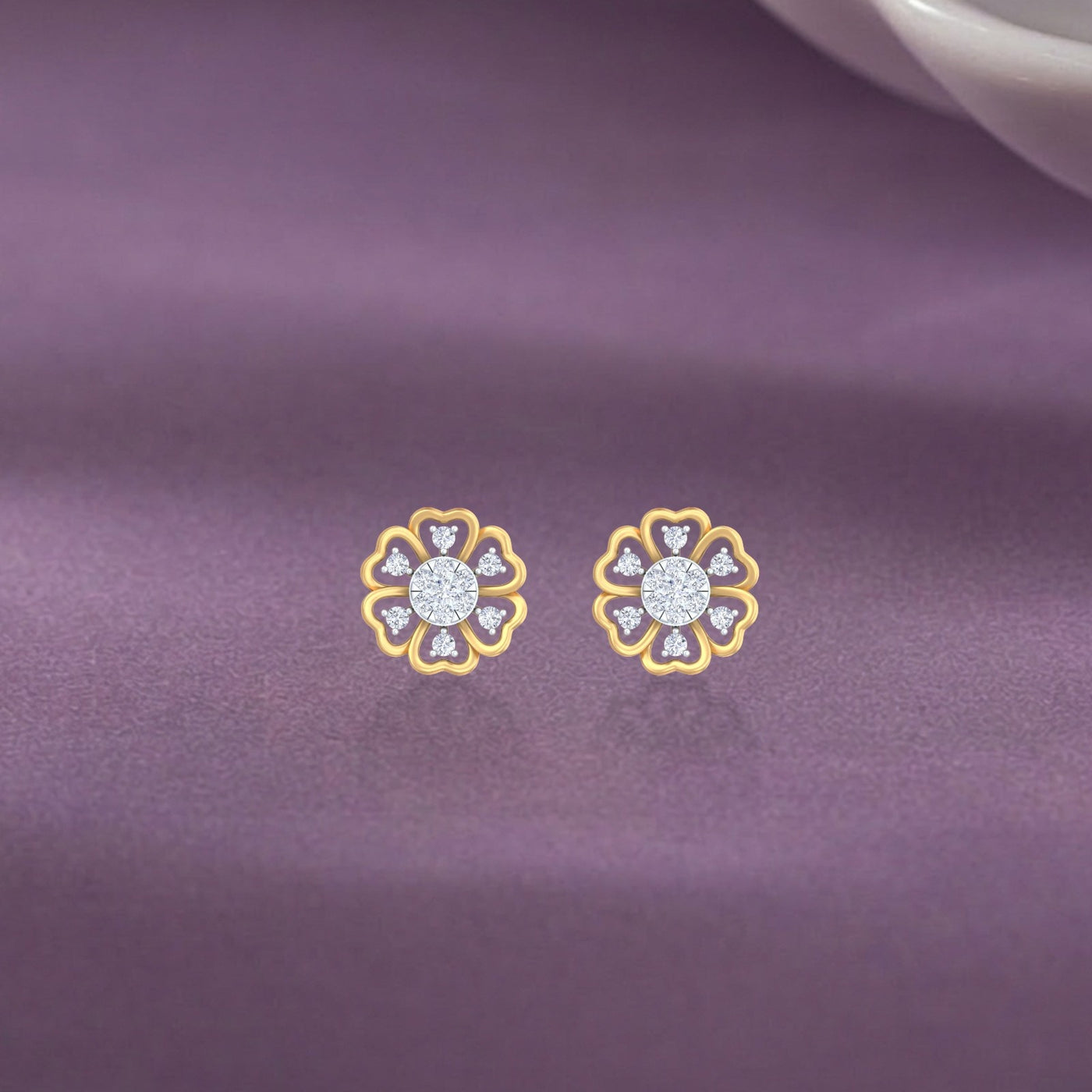 Gold and diamond with floral-design stud earrings on a purple fabric background.