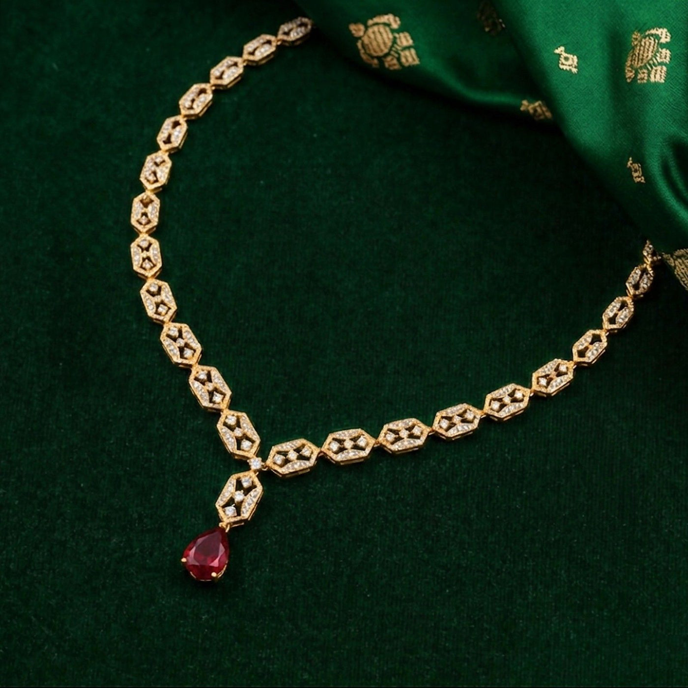 Gold necklace with a red gemstone on a green fabric background.