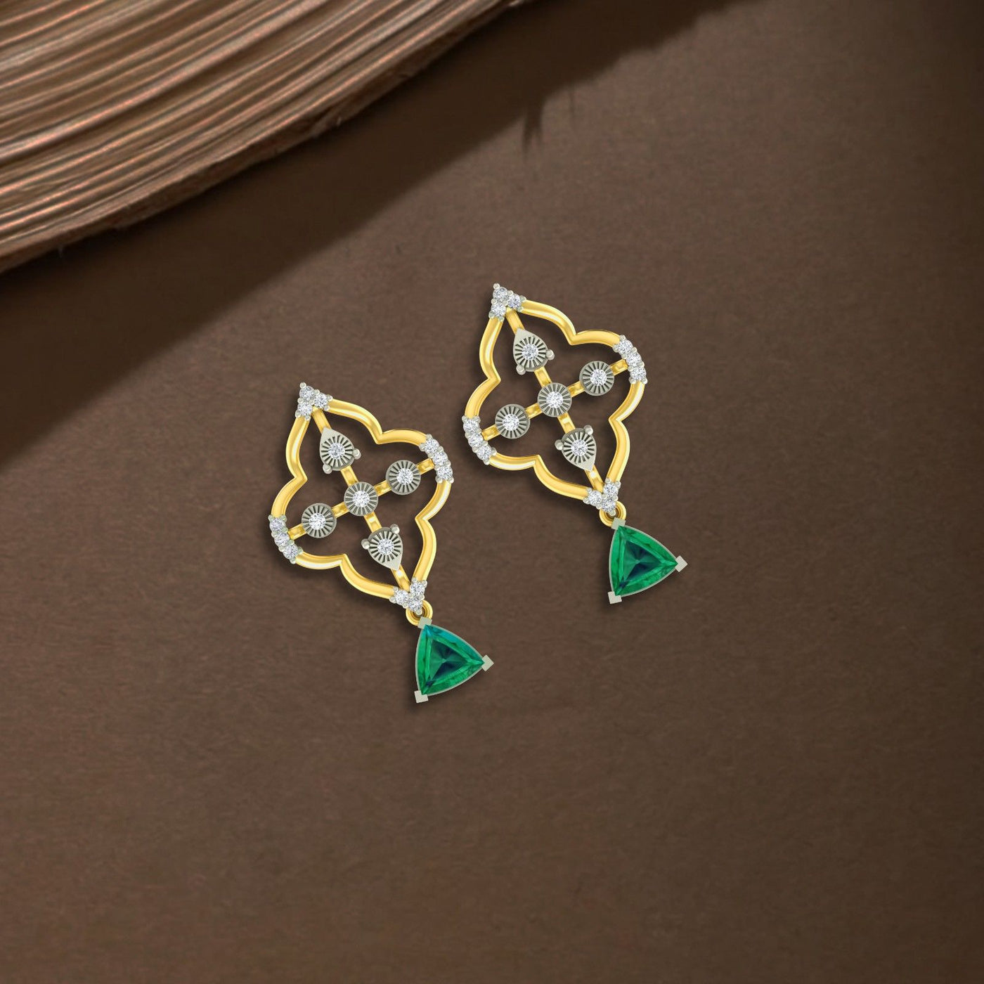 Gold and diamond drop earrings with emerald gemstones on a brown background.