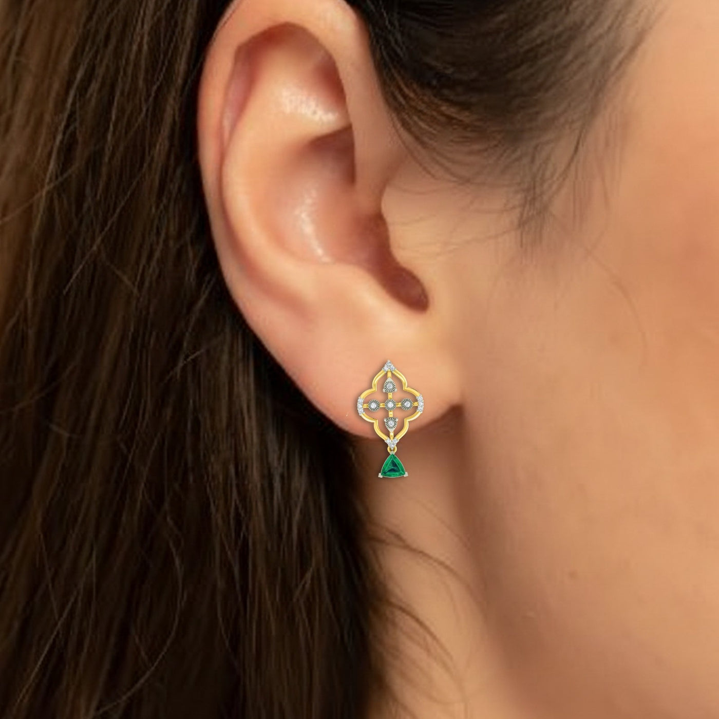 Close-up shot of a gold and diamond drop earrings with emerald gemstones.
