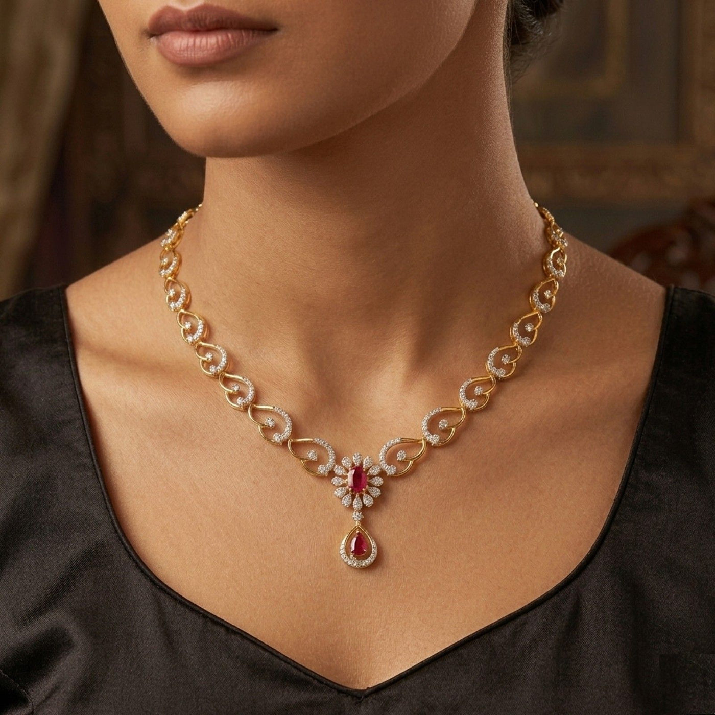 A close-up of a woman wearing a gold and diamond necklace with a red teardrop gemstone.