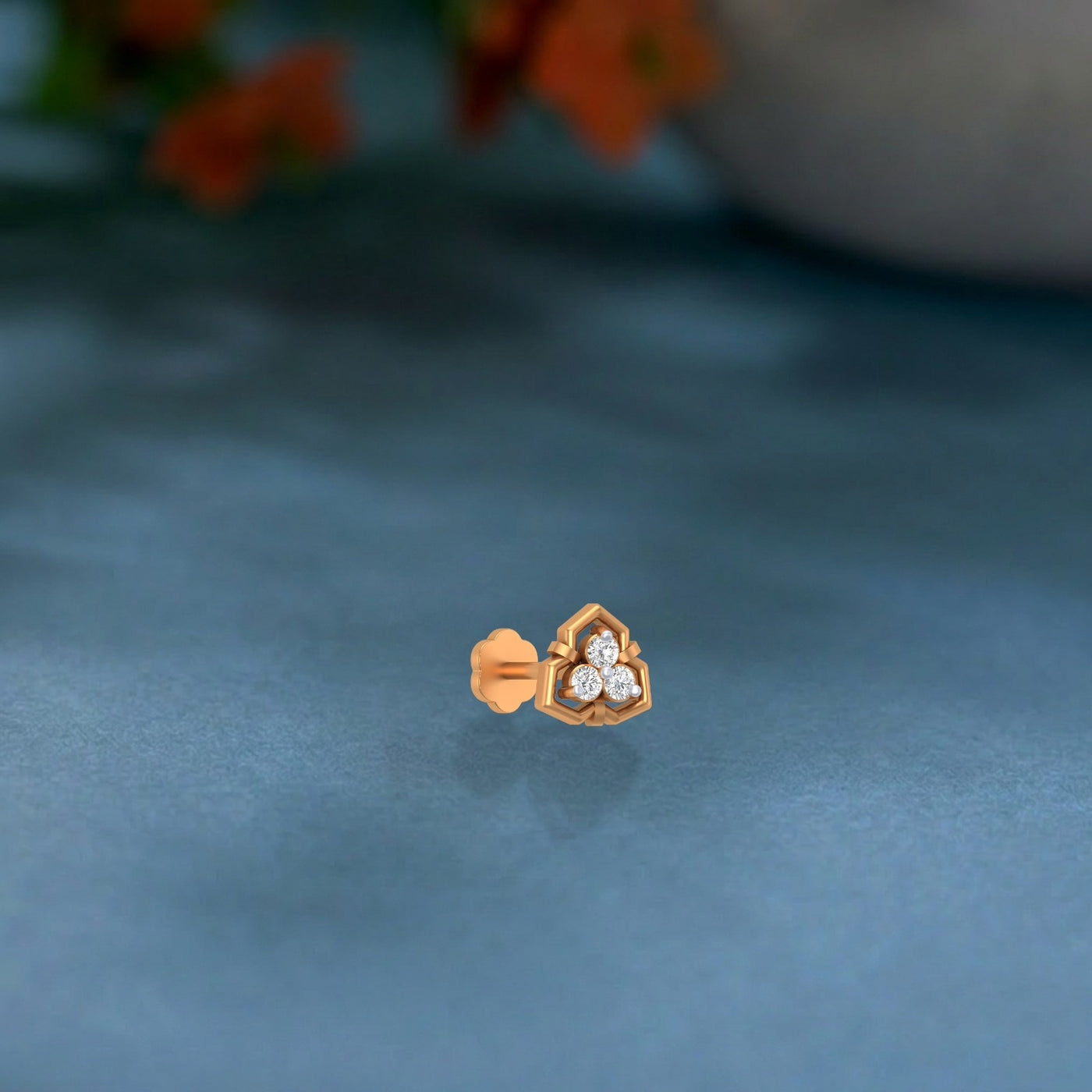 Yellow gold and diamond stud nose pin with a heart design on a textured blue surface