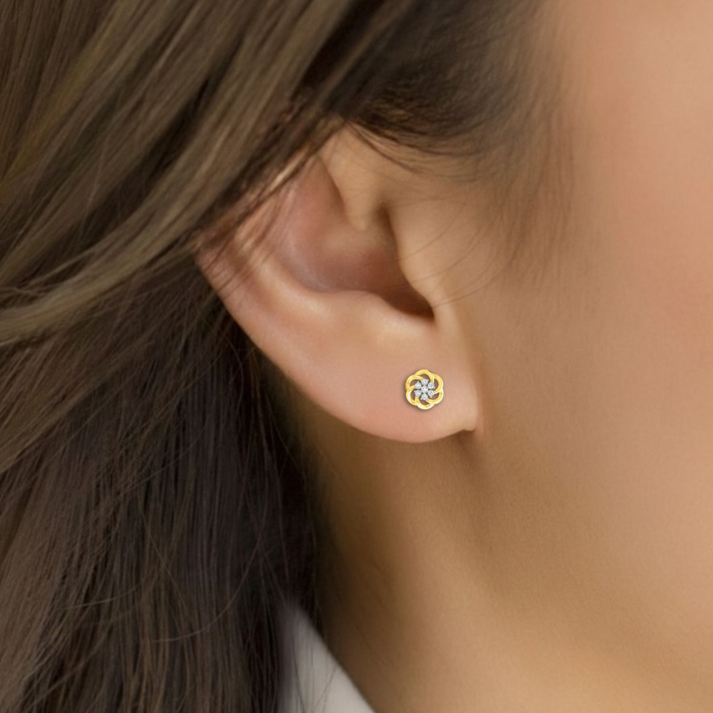 Close-up of an ear wearing a gold and diamond floral earring with dark hair and skin background.
