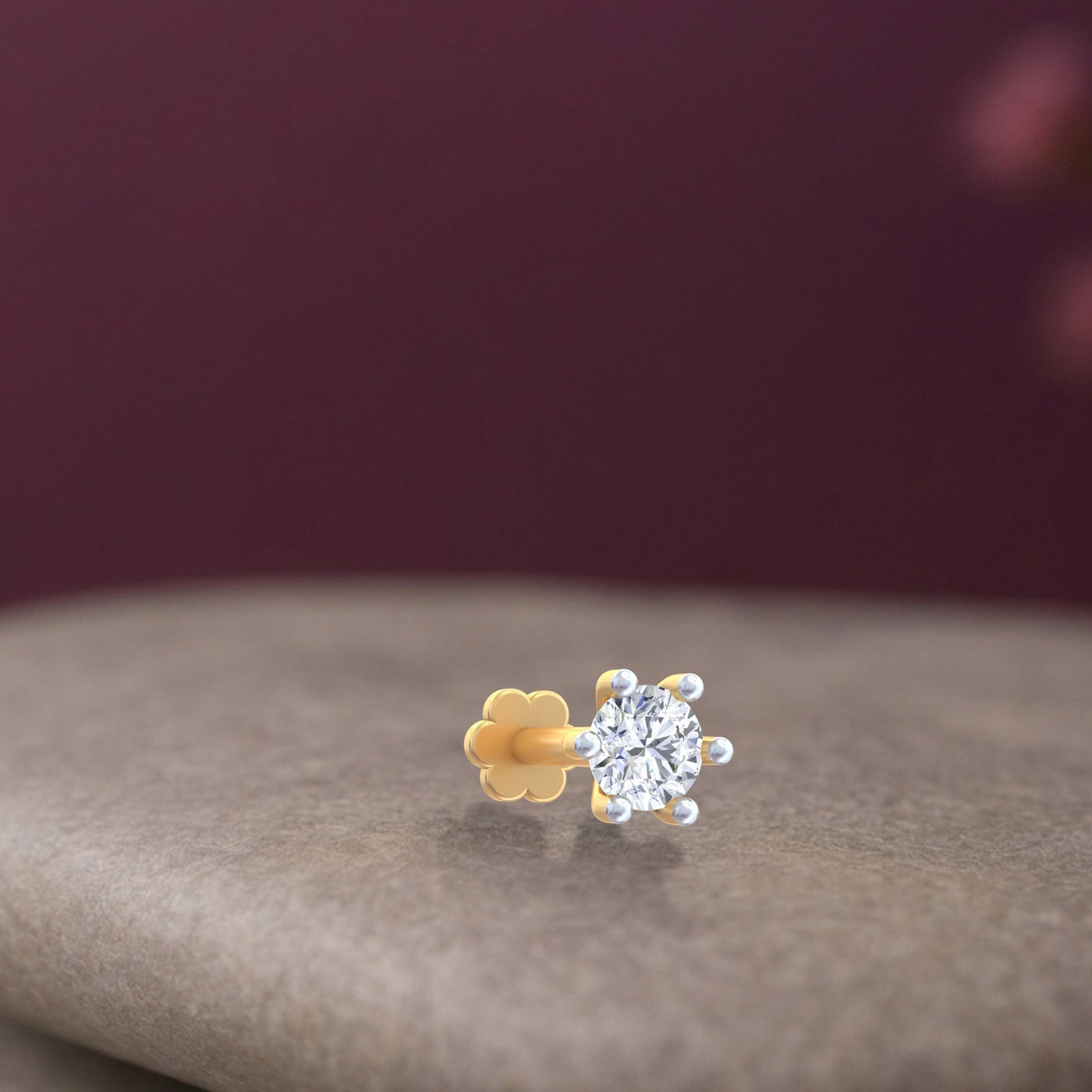 Gold and diamond stud nose pin on a textured surface with a blurred background