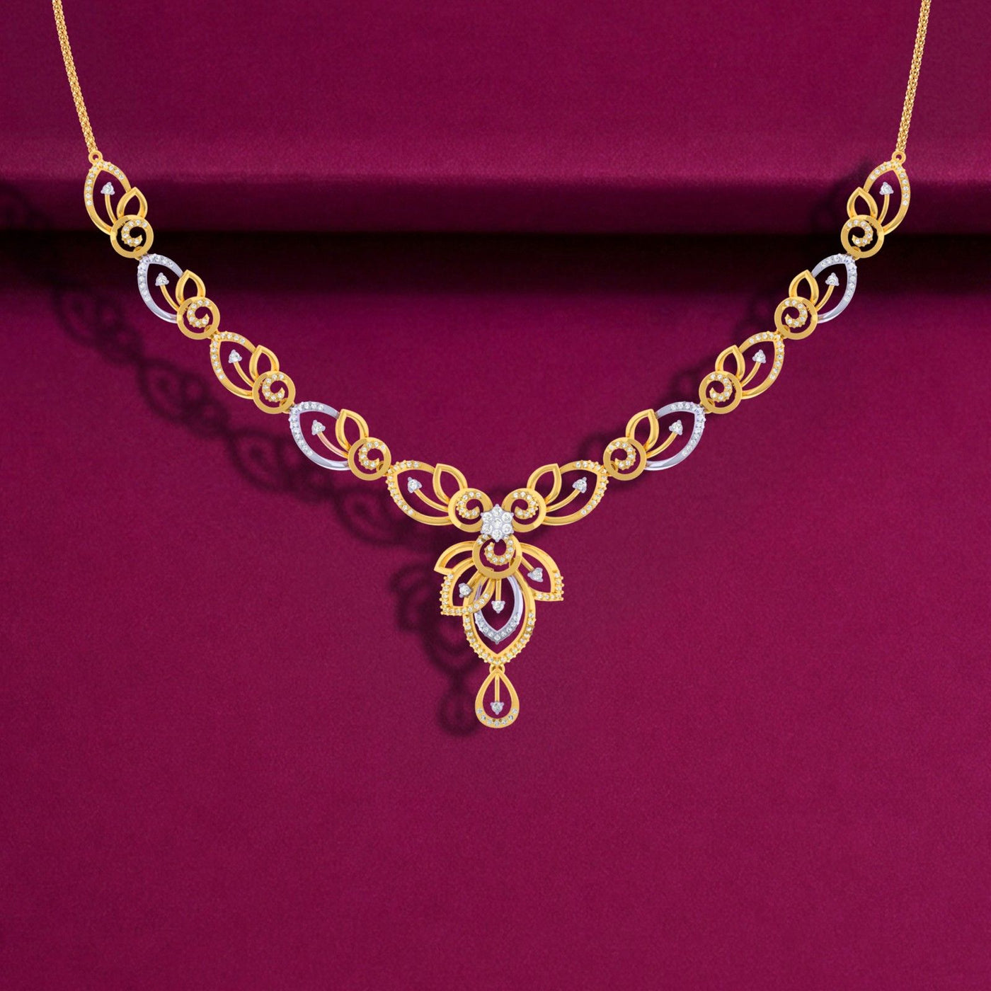 A two-tone yellow and white gold necklace featuring diamond-accented swirl and leaf motifs, displayed against a deep maroon background.