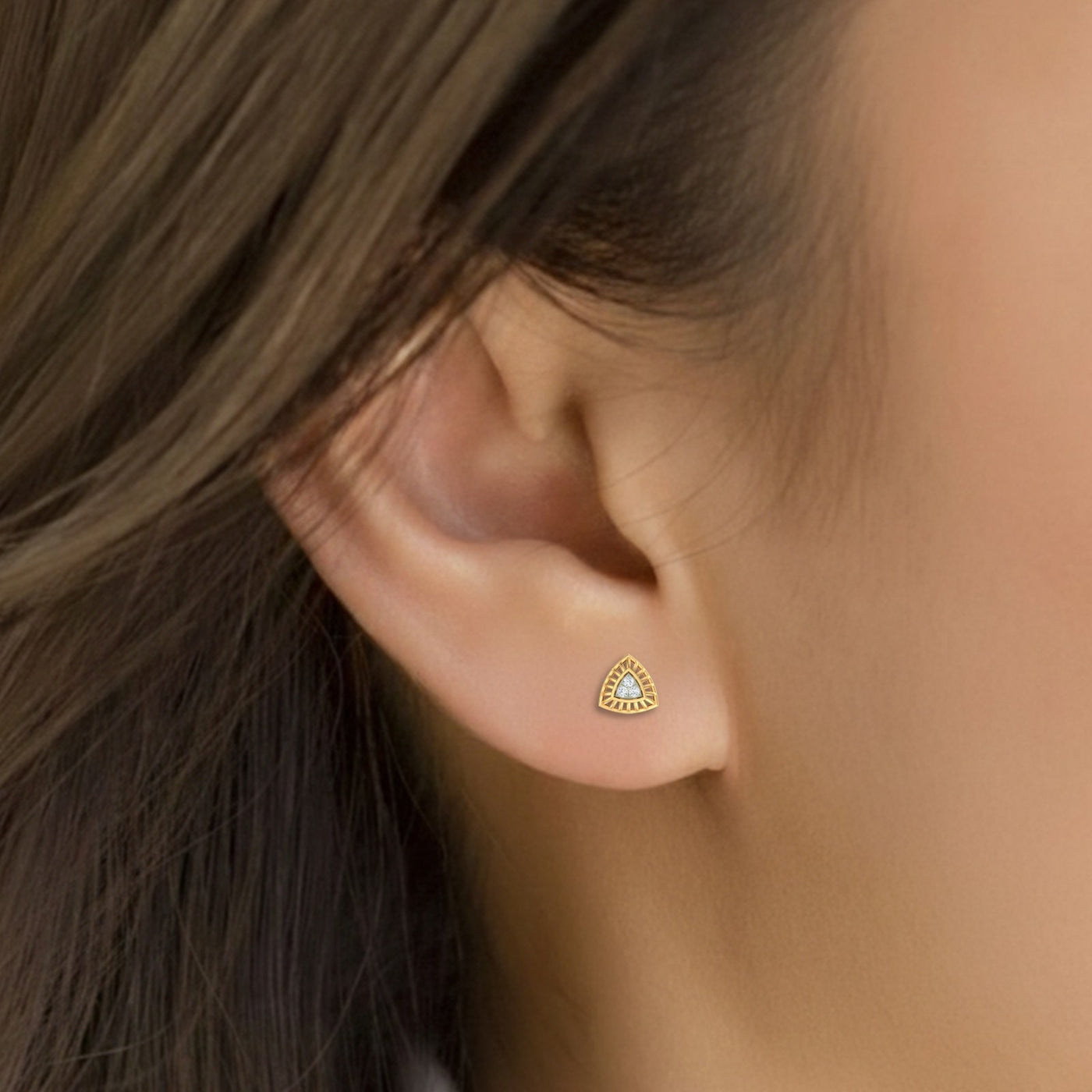 Close-up of an ear wearing a gold and diamond stud earring.