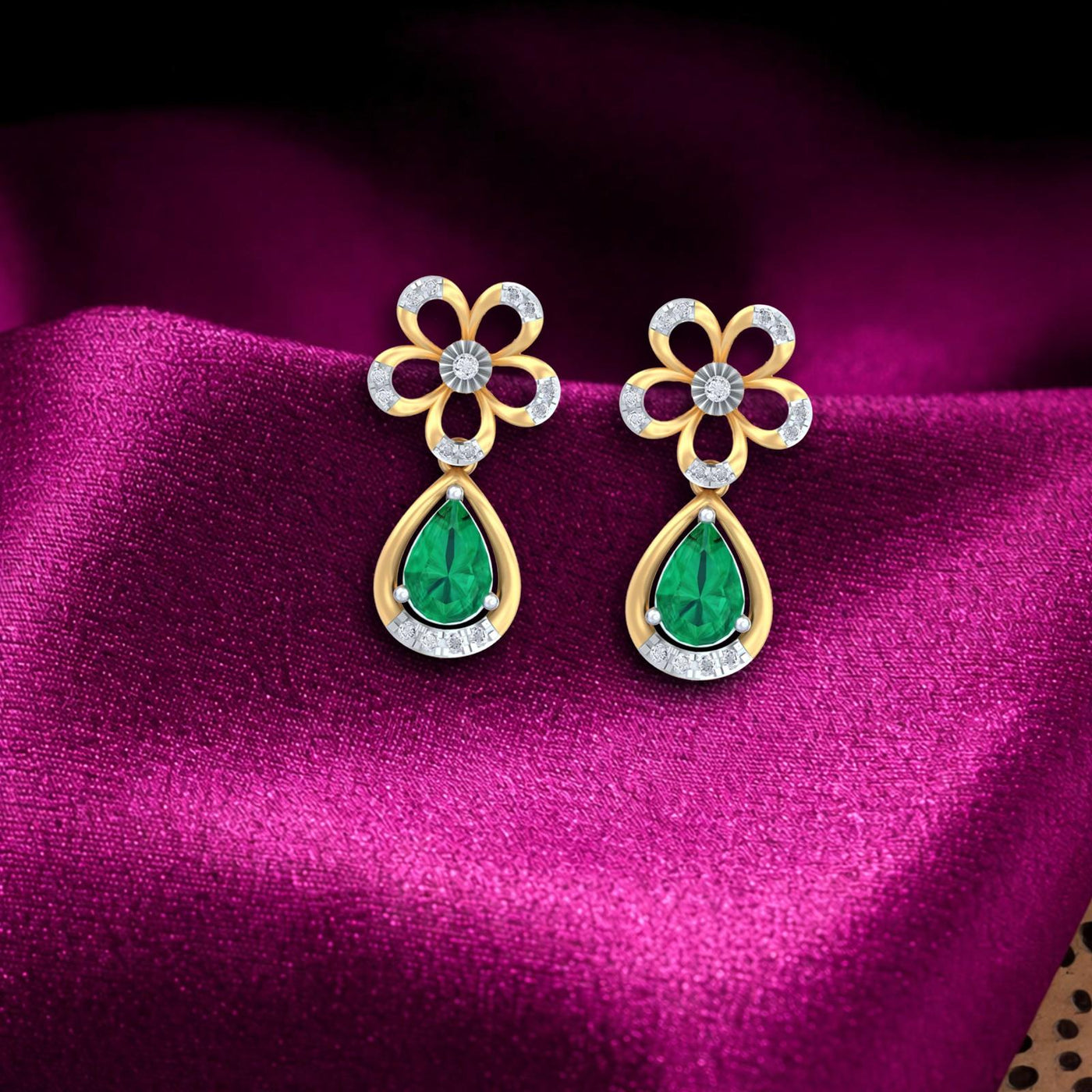 Gold and diamond drop earrings with emerald gemstones on a magenta fabric background
