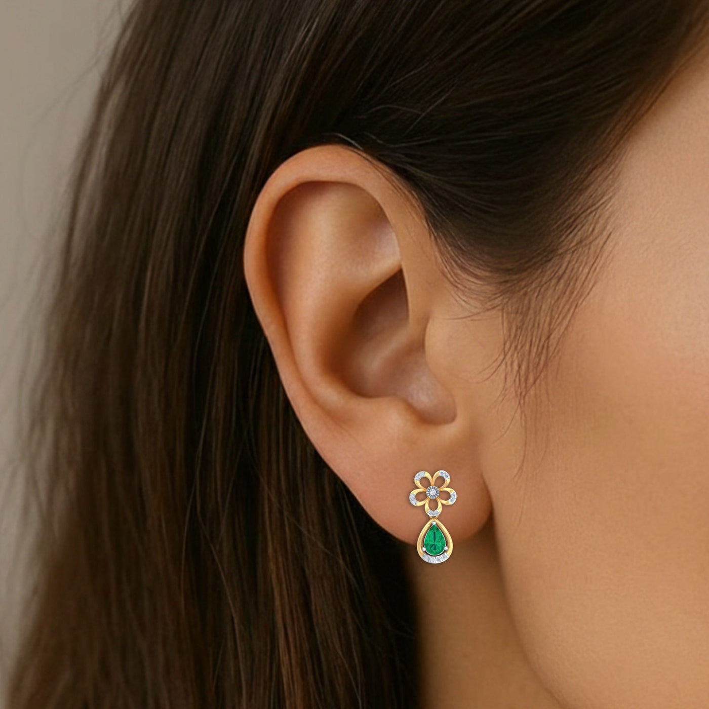 A close-up of a model's ear wearing a gold flower drop earring with a green teardrop gemstone.