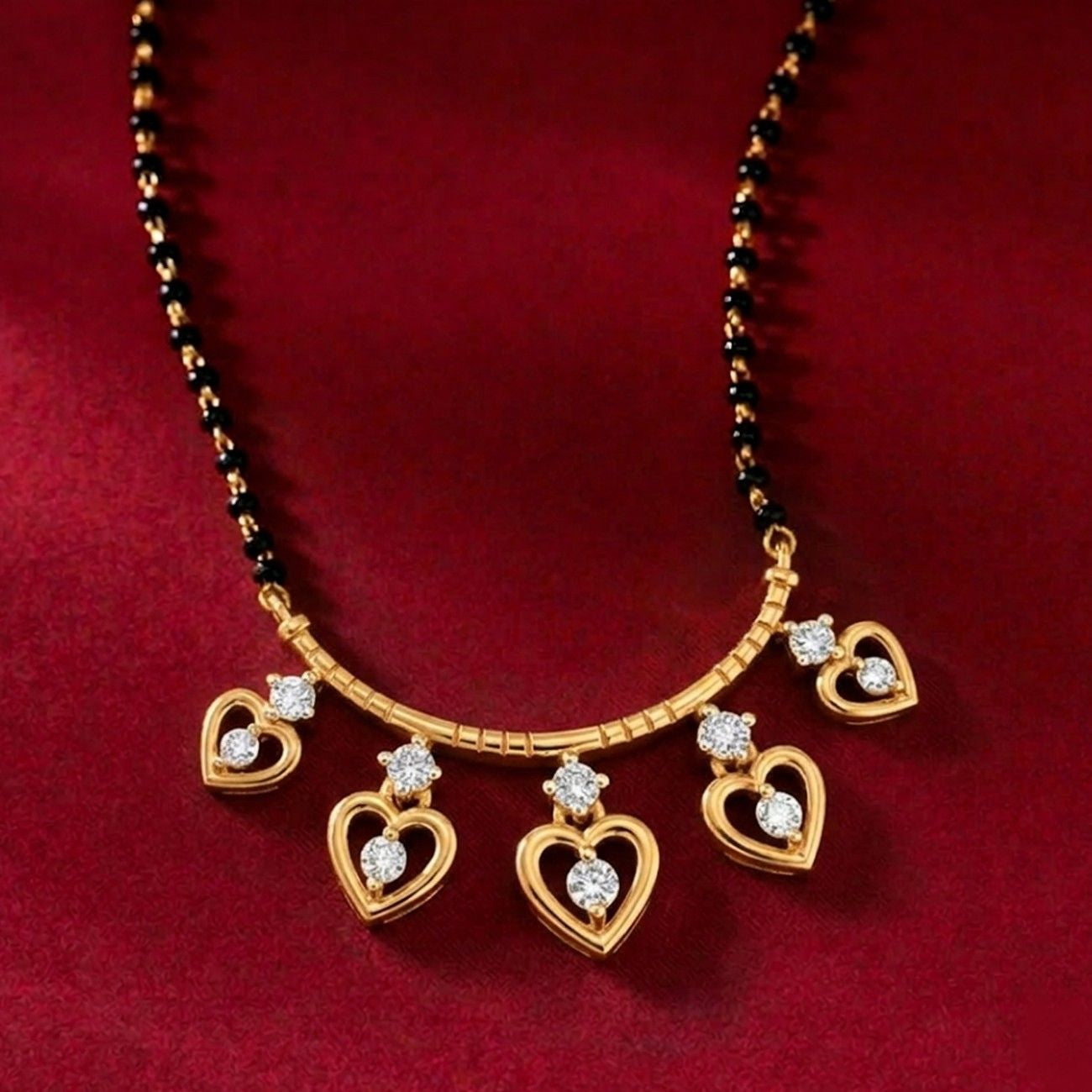 Yellow gold heart charm gold and diamond mangalsutra featuring five dangling heart charms, each adorned with set against a plain red background.