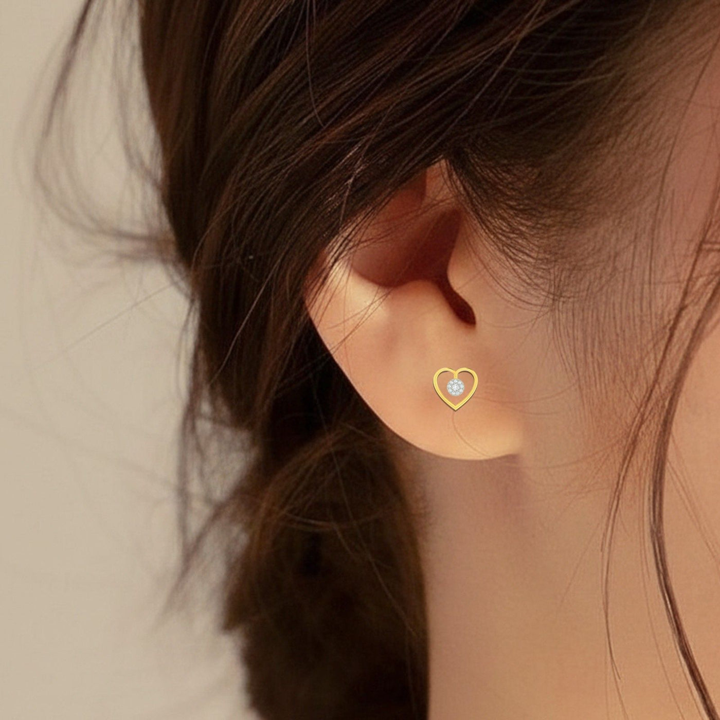 Gold and diamond heart-shaped earring worn by a person.